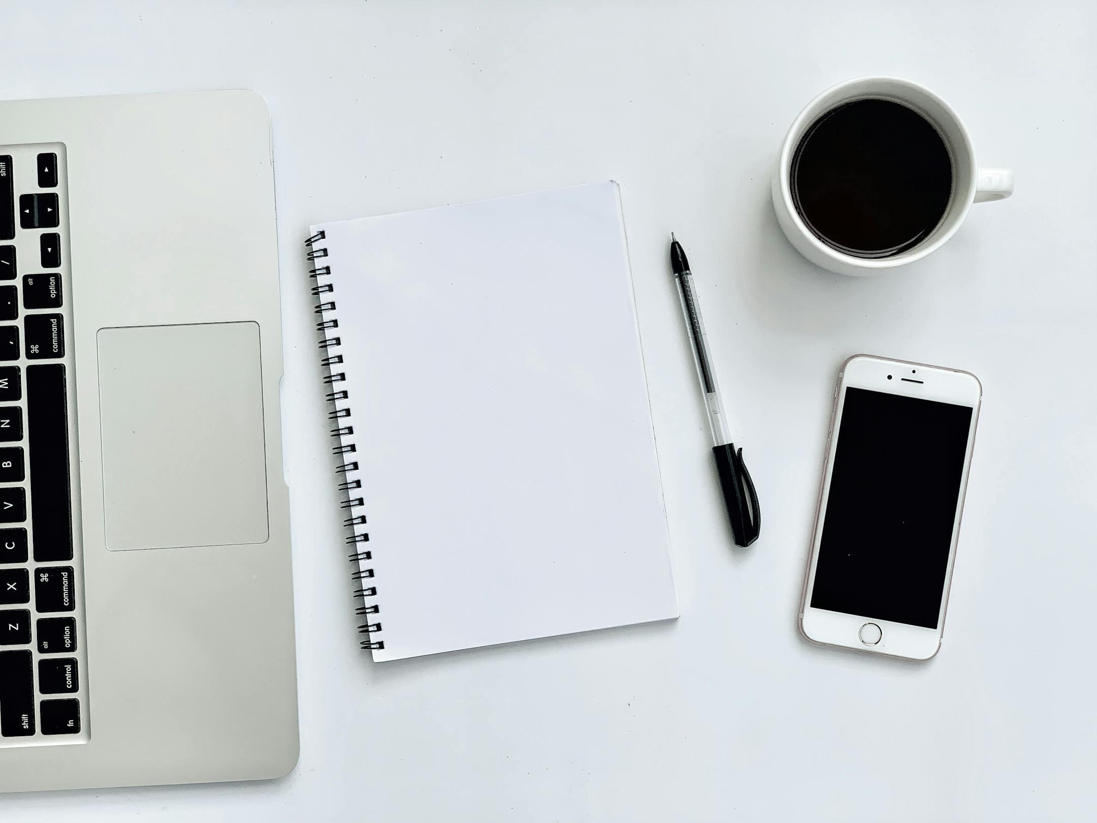 A clean and simple workspace featuring a laptop, smartphone, and coffee mug on a white desk.