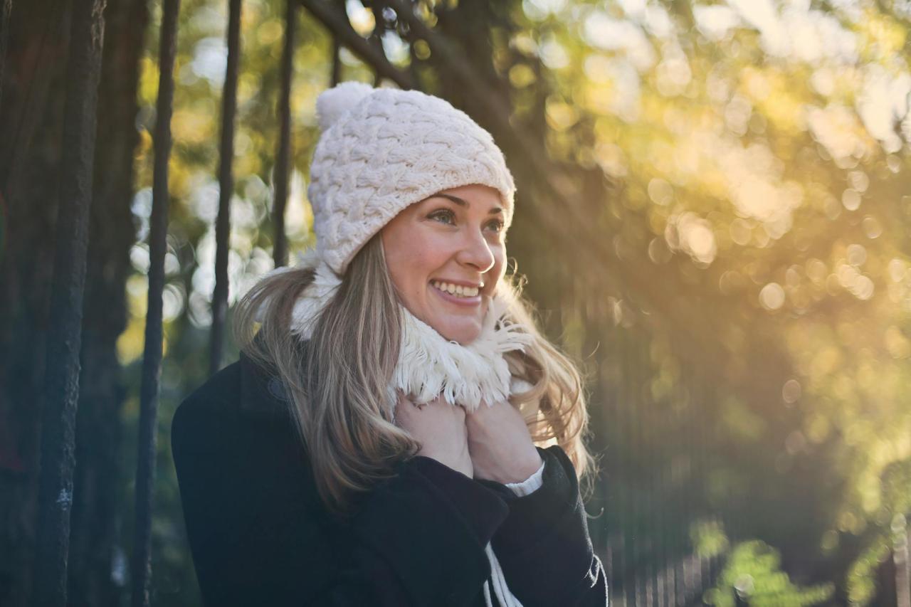 Cheerful woman enjoying a sunny winter day outdoors, wearing a cozy scarf and knit cap.
