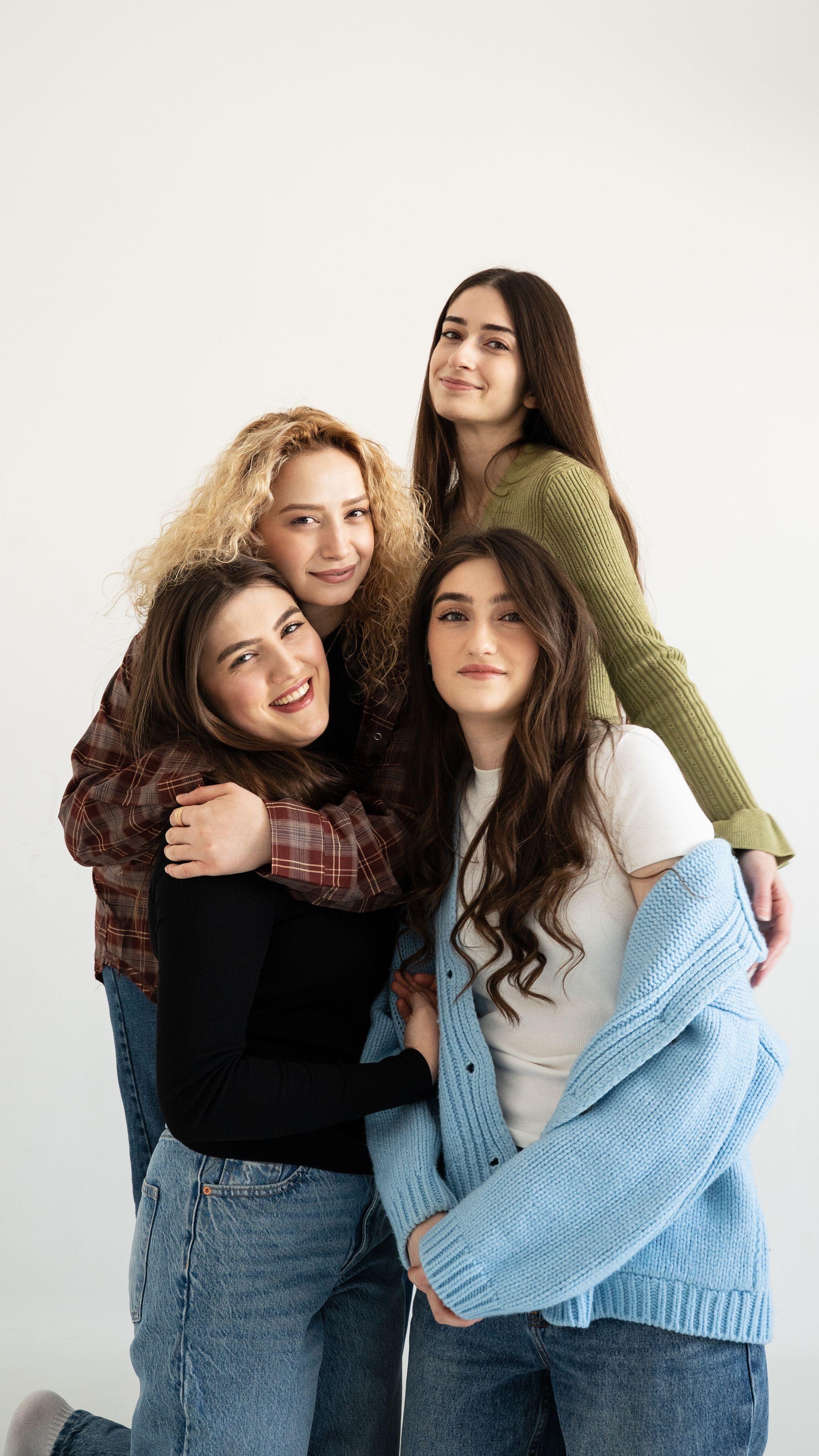 Four smiling teenage girls embracing joyfully inside a bright room.