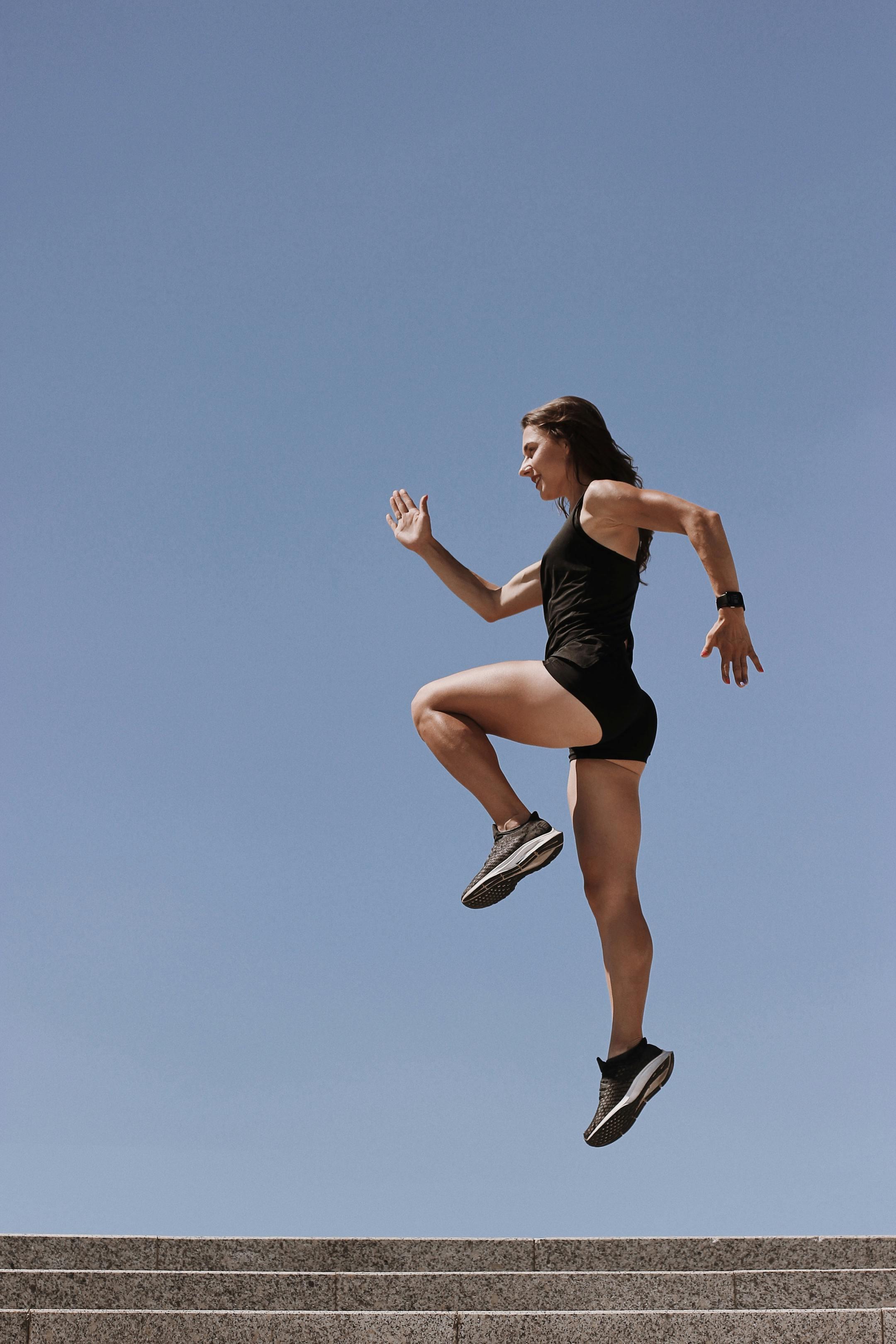 A woman in athletic wear energetically leaps up stairs against a clear blue sky.