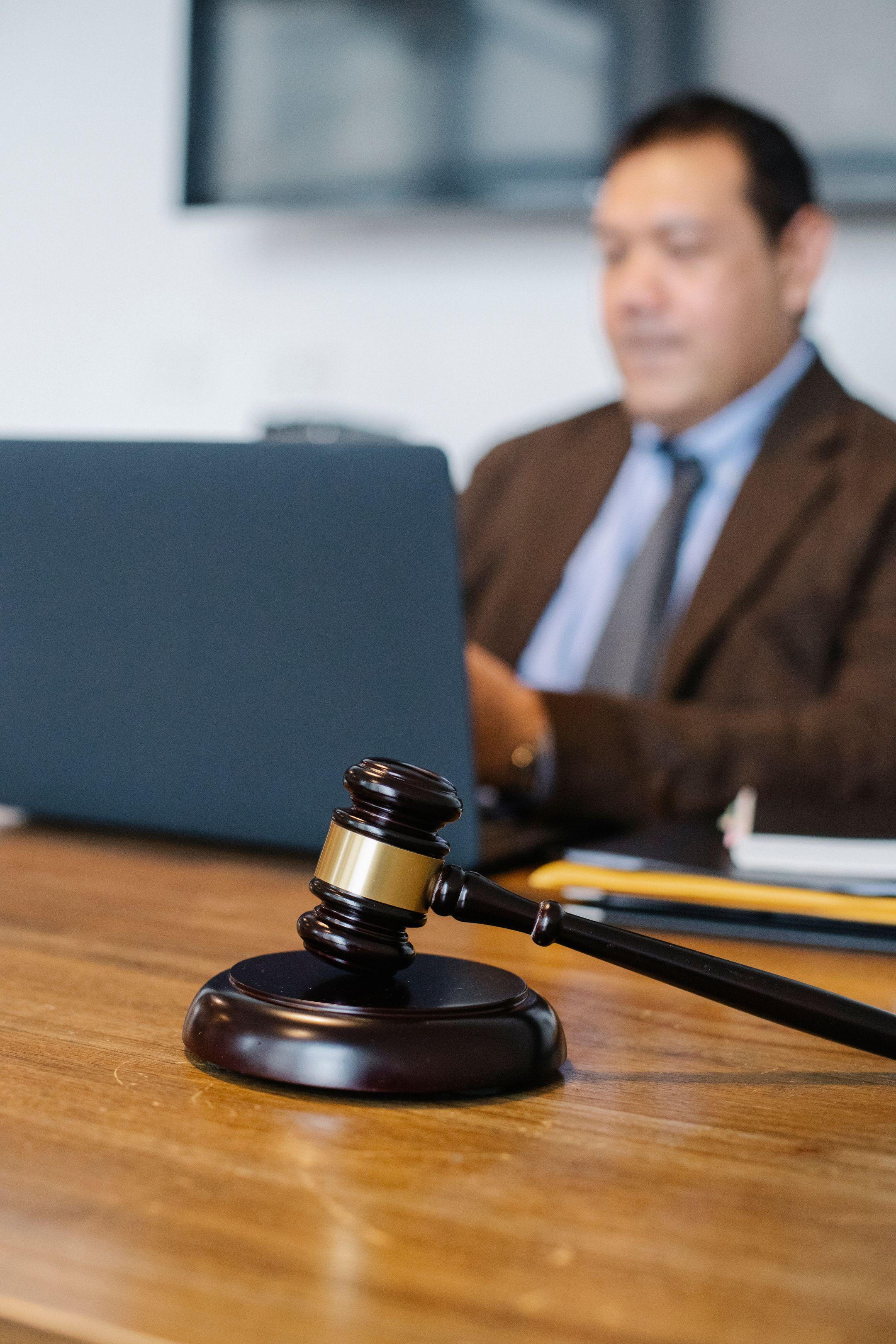 Blurred male lawyer in formal suit sitting at table with modern netbook and decorative gavel