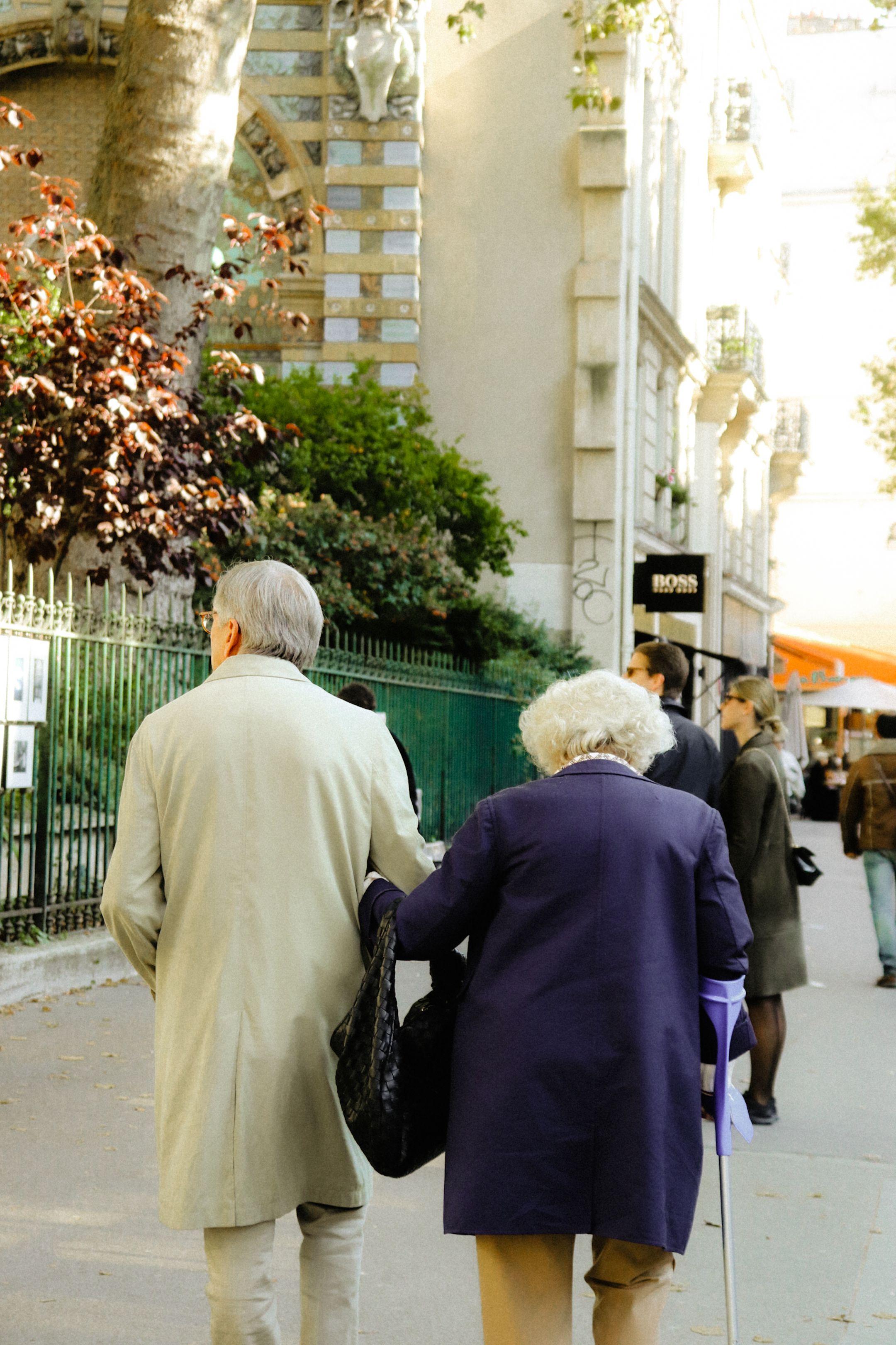 A senior couple strolls arm-in-arm on an urban sidewalk, showcasing companionship and urban life.