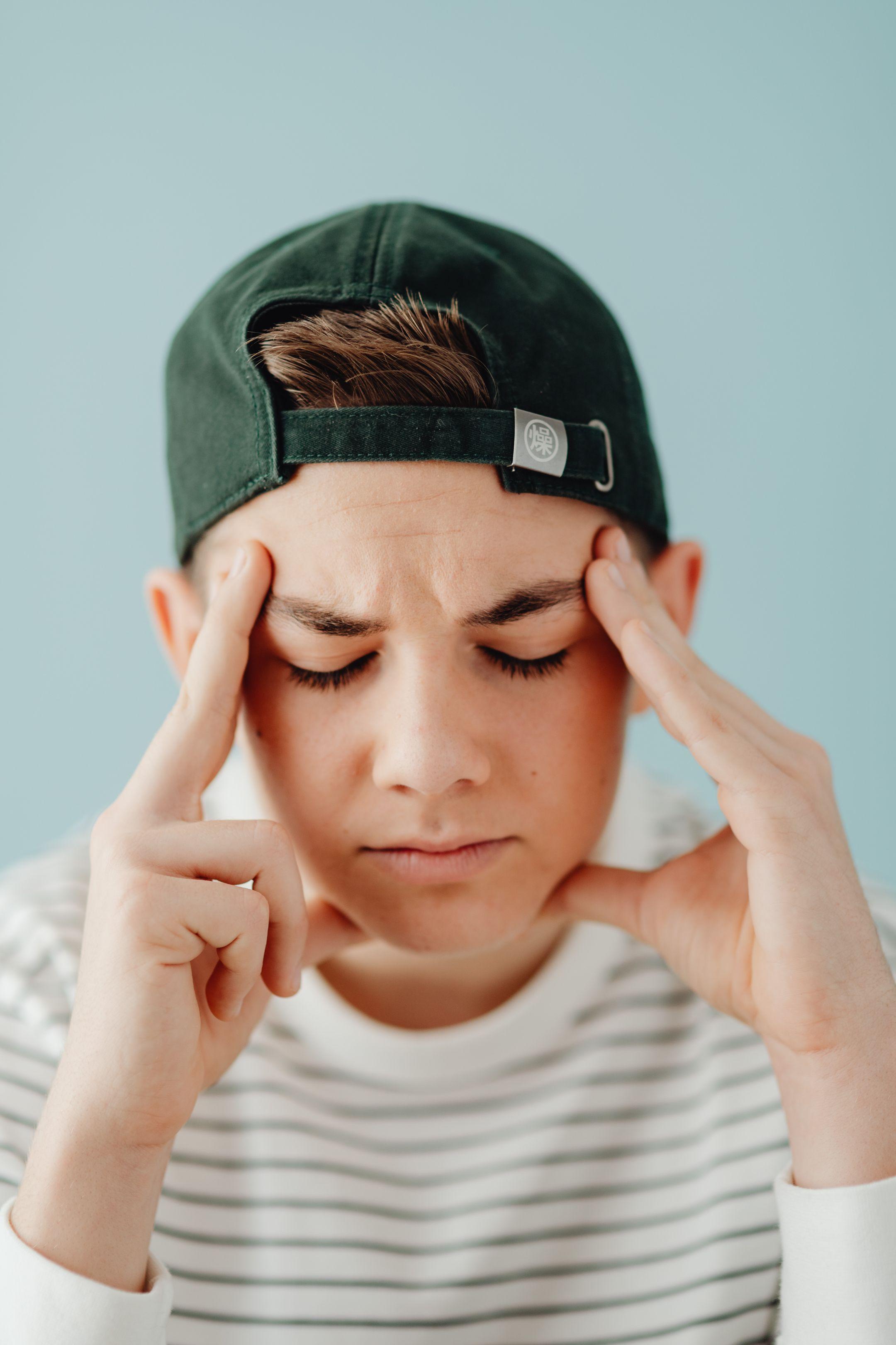 A close-up portrait of a teenage boy with eyes closed, wearing a backwards cap, expressing thoughtfulness.