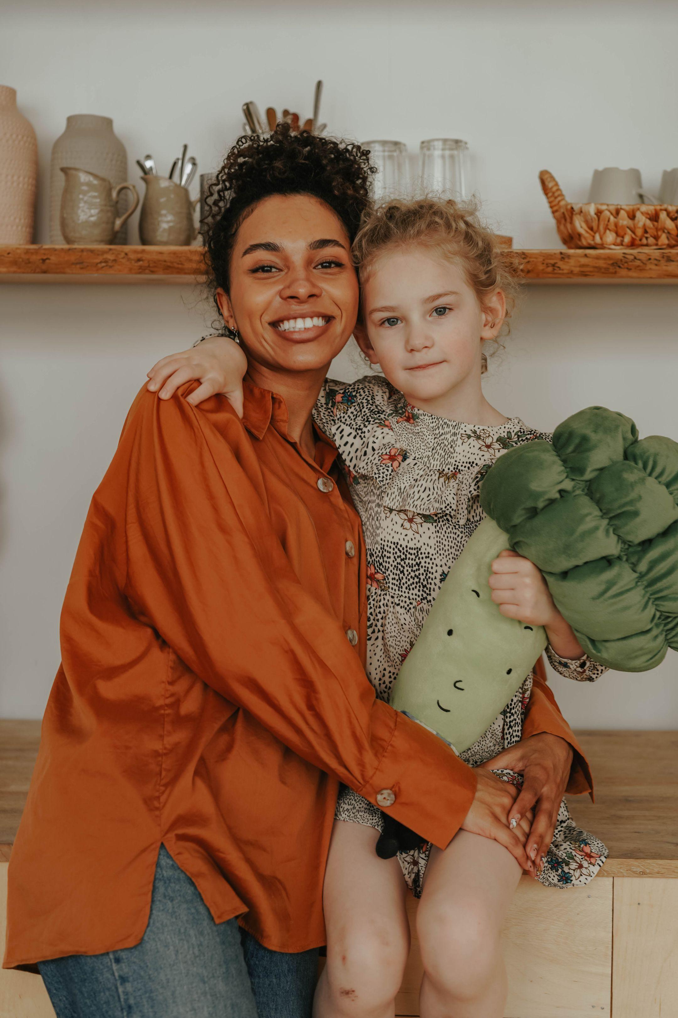 Mother and daughter smiling indoors, bonding with a broccoli toy.