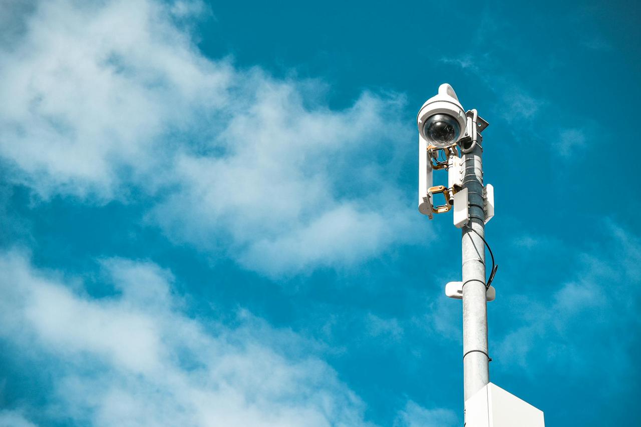 Close-up of a surveillance camera on a pole under a clear blue sky.