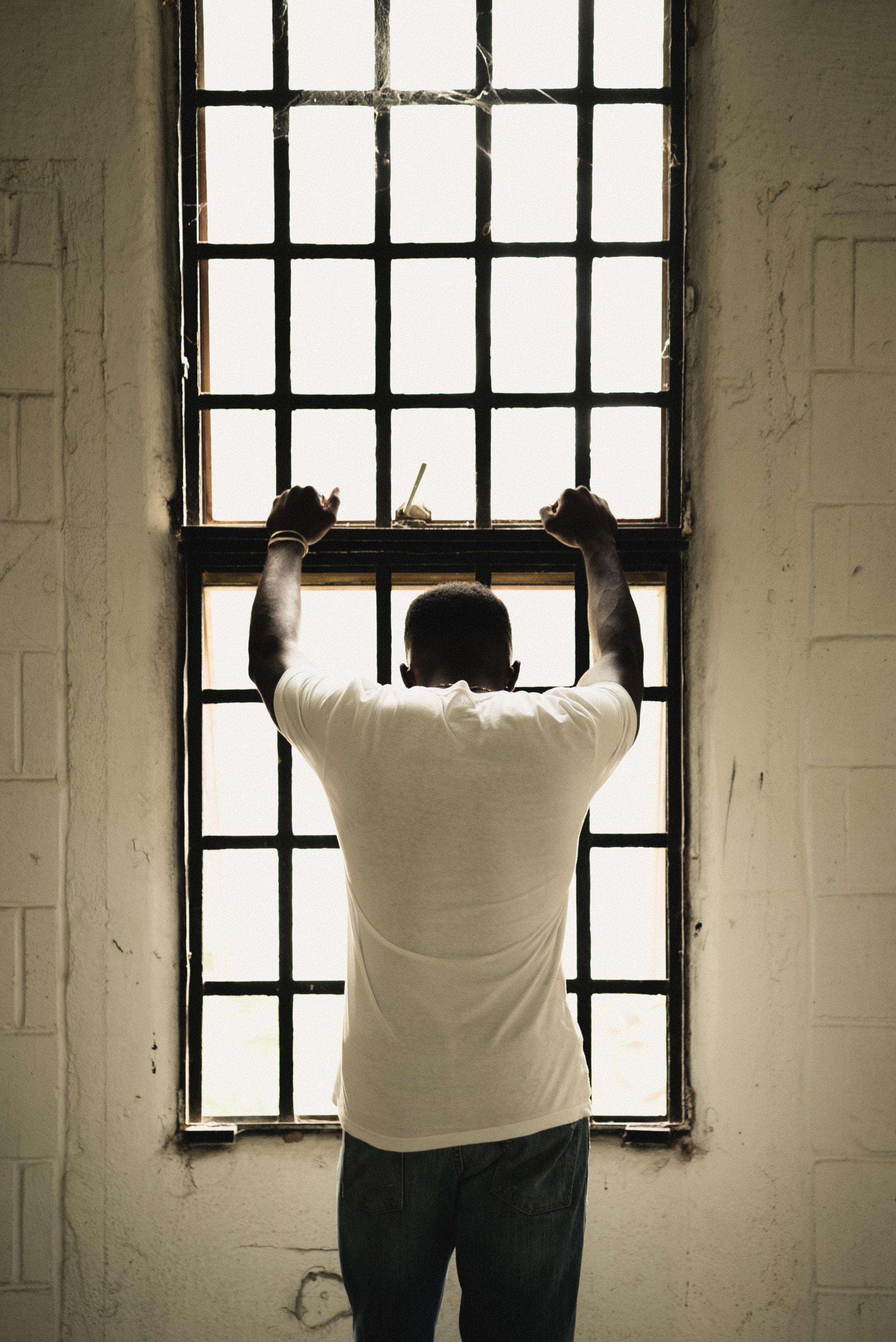 A man standing against a window with bars covering it. Without a criminal defense attorney in Tampa, FL, your chances are slim to none.