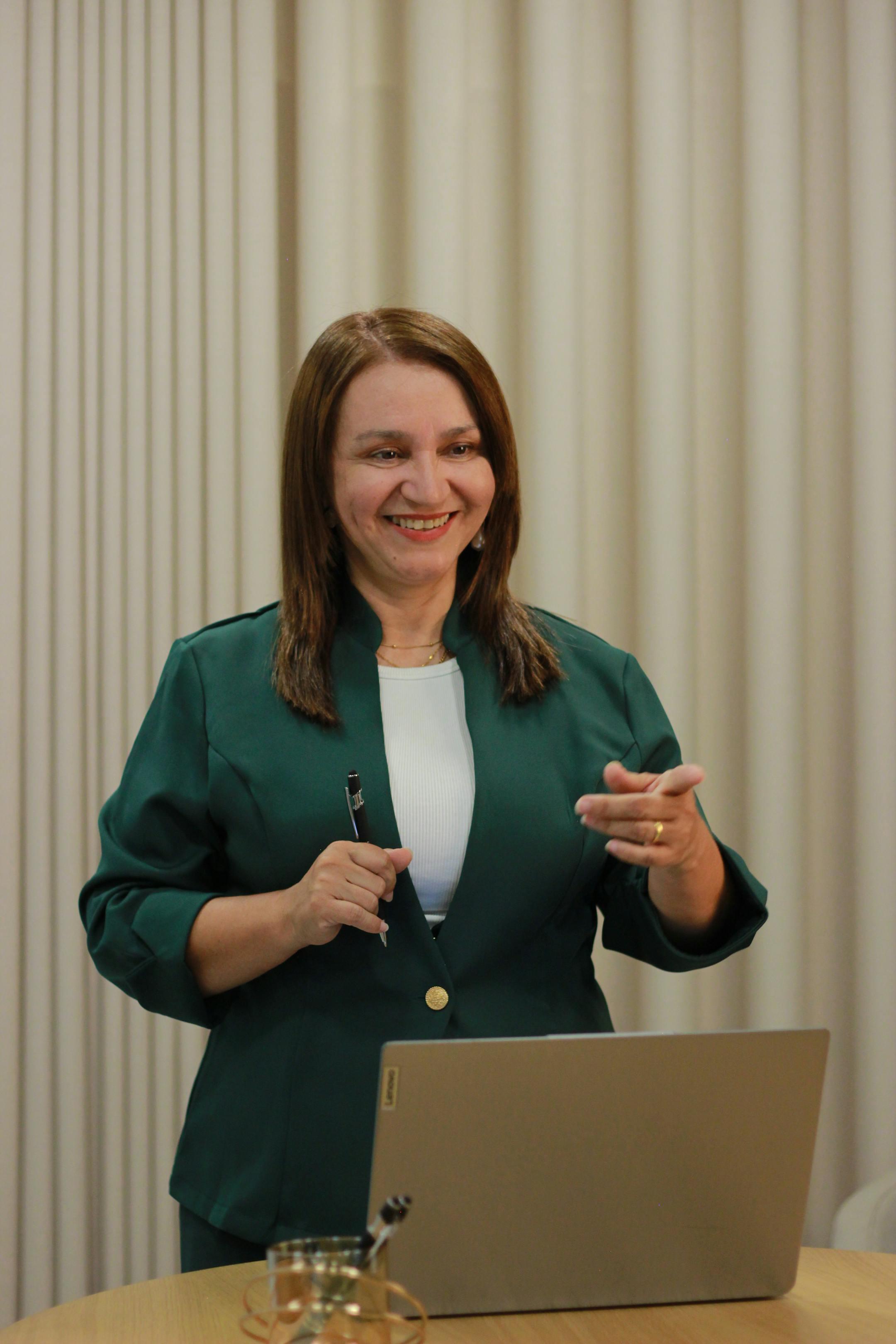 Confident woman in a green blazer giving a presentation in a modern office setting.
