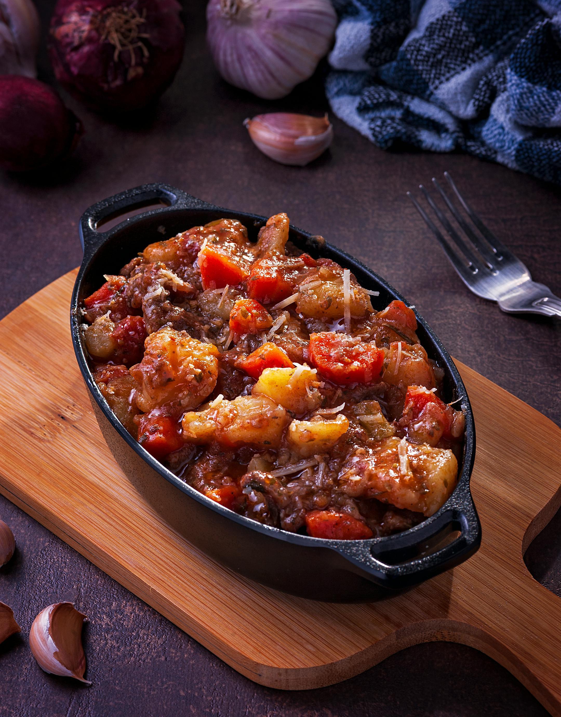 Delicious homemade beef stew with vegetables in a black cast iron dish on a wooden board.