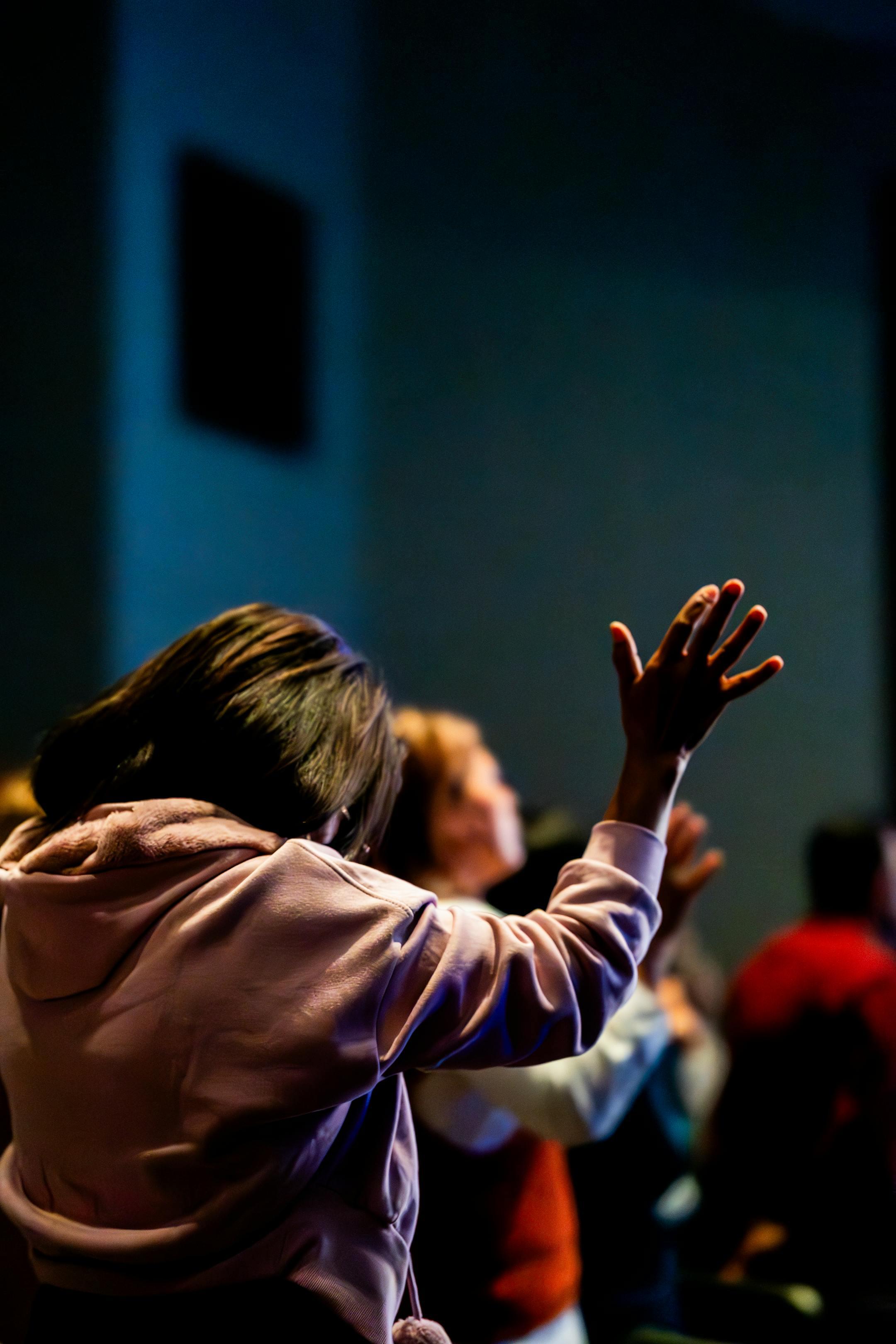 A group of people raising their hands in a spiritual gathering, immersed in prayerful worship.