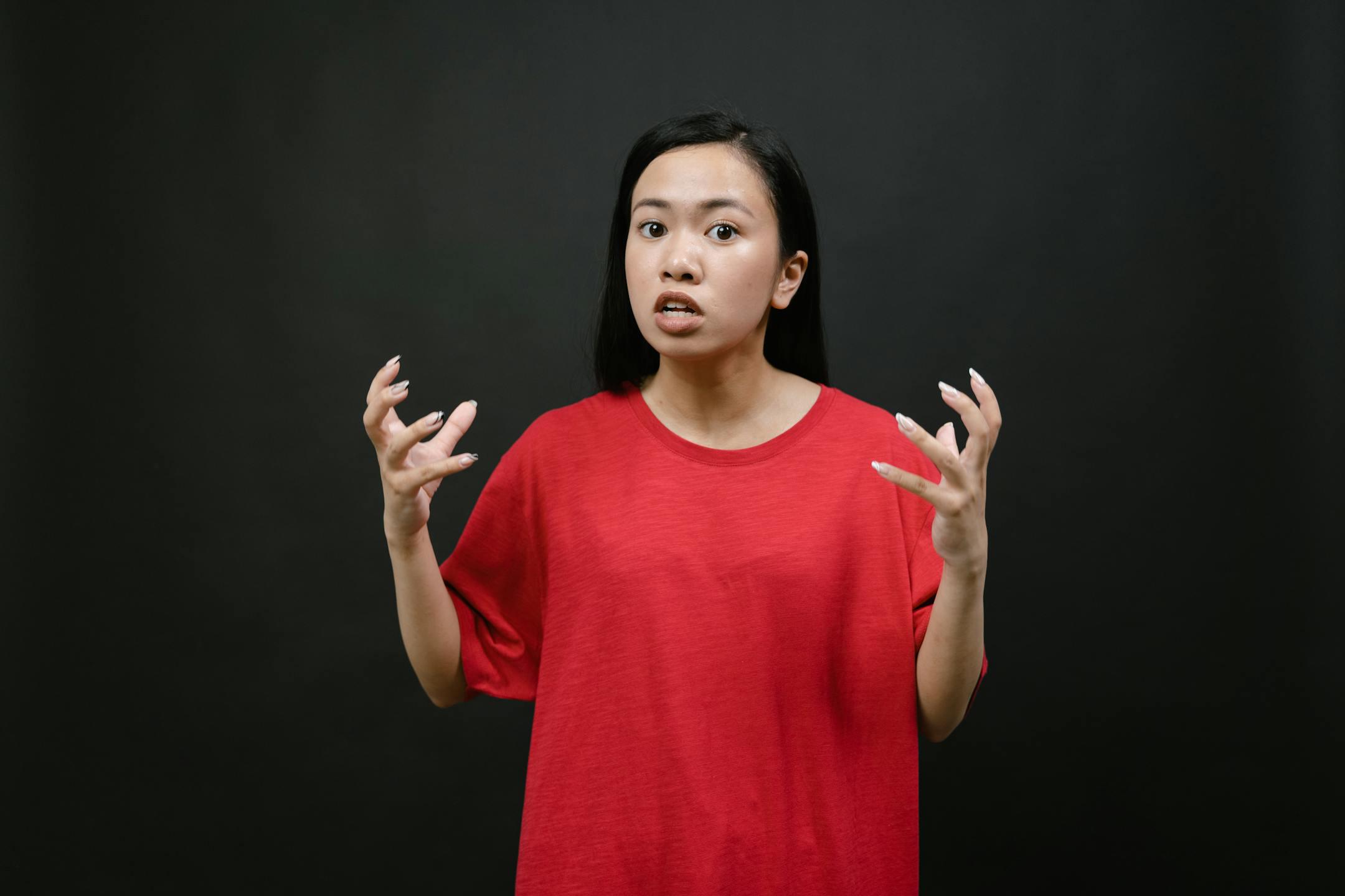An Asian woman in a red shirt expressing frustration or surprise in a studio setting.
