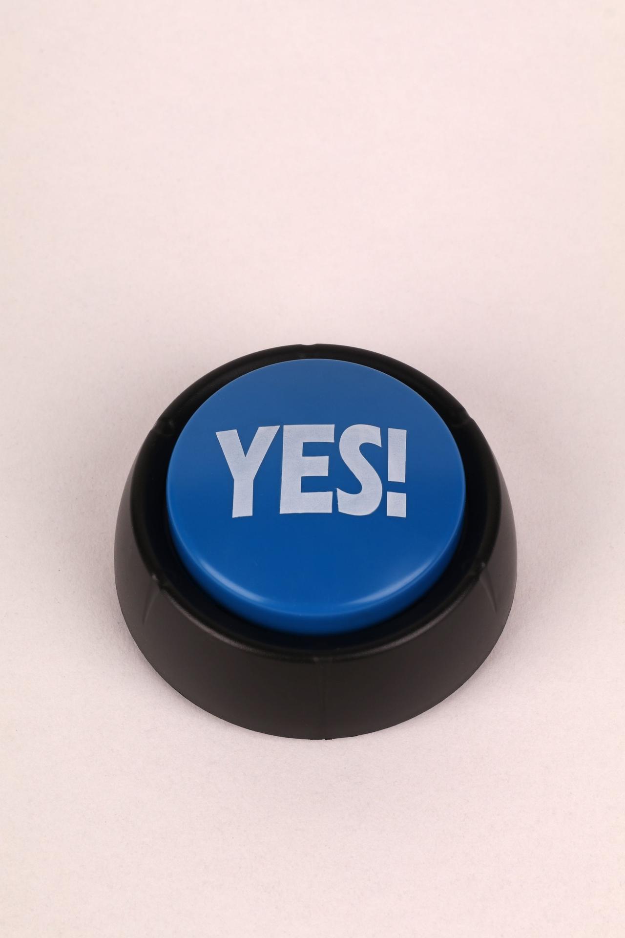 Close-up of a blue button with 'Yes!' text on a beige background, perfect for communication themes.