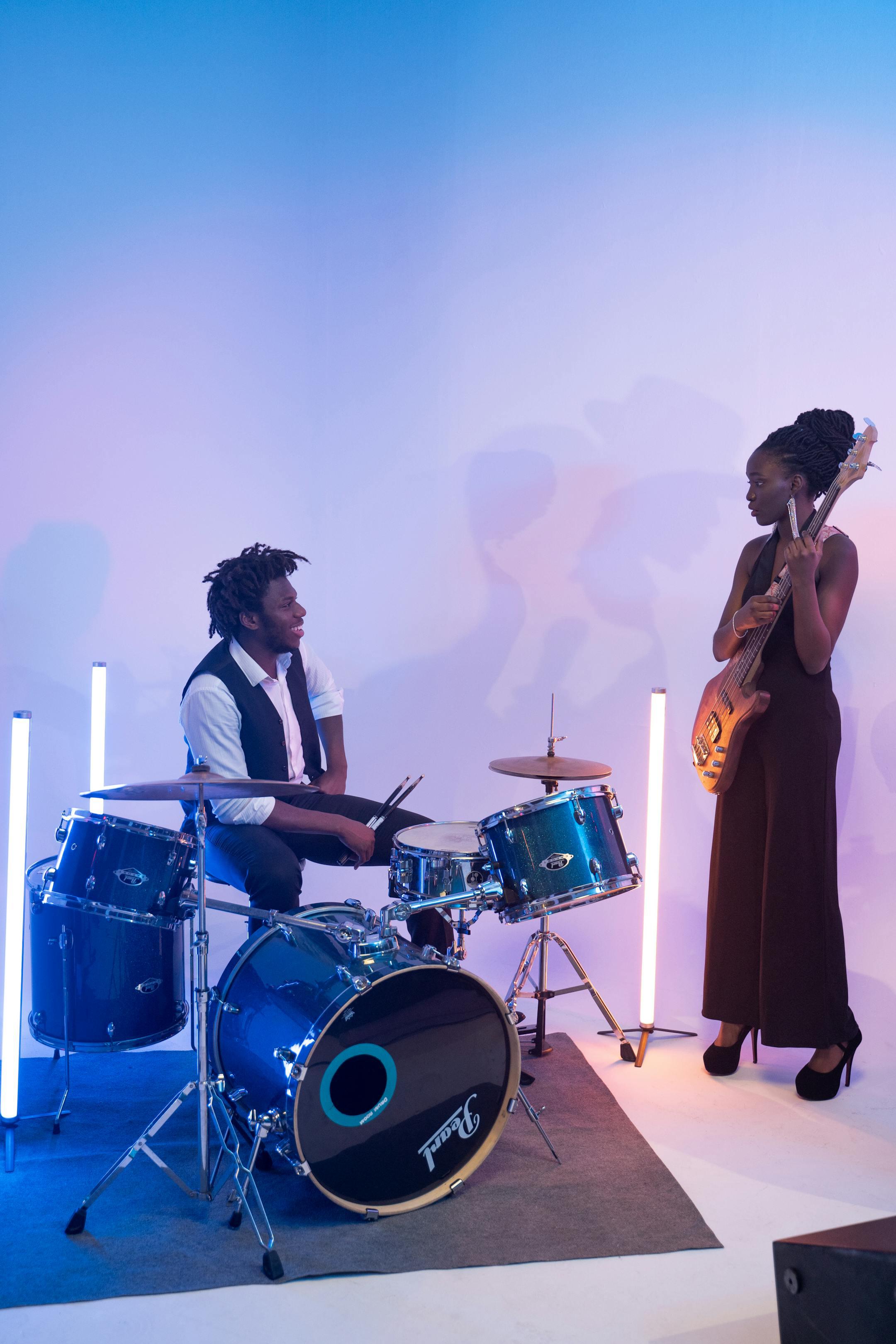 Musicians performing with drums and guitar in a studio with vibrant lighting.