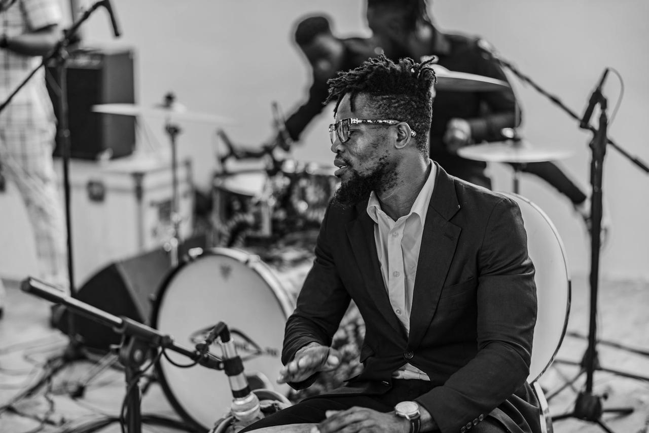 African musician playing drums in a band setting, black and white photo.