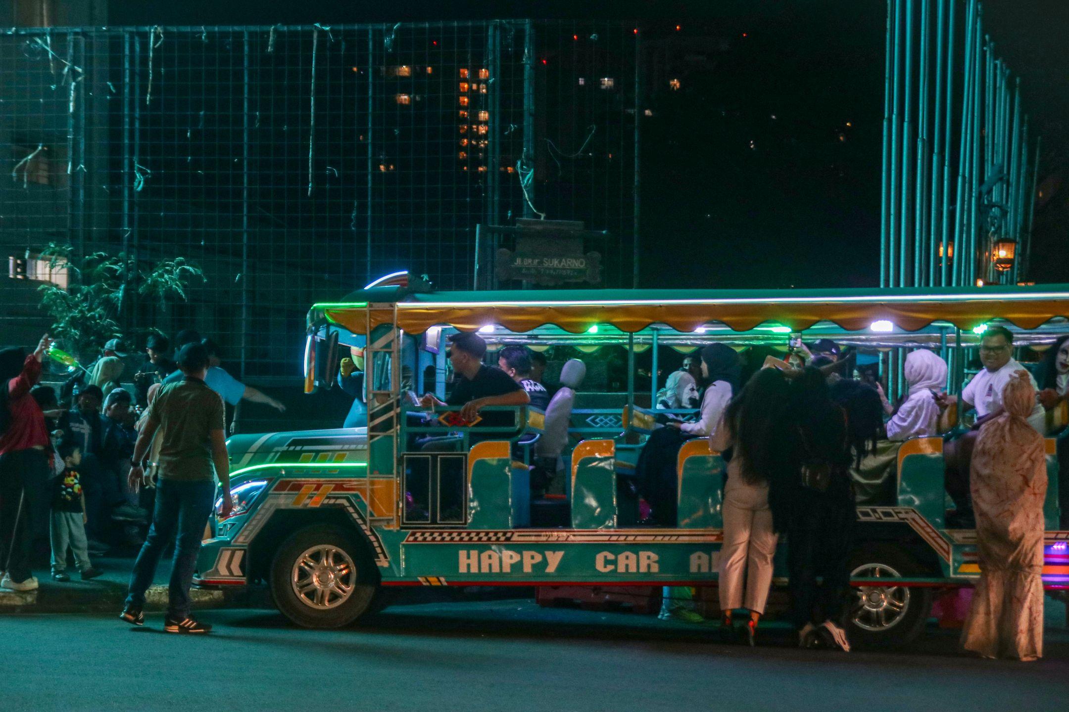 A vibrant night scene with a colorful tour bus and passengers in an urban environment.