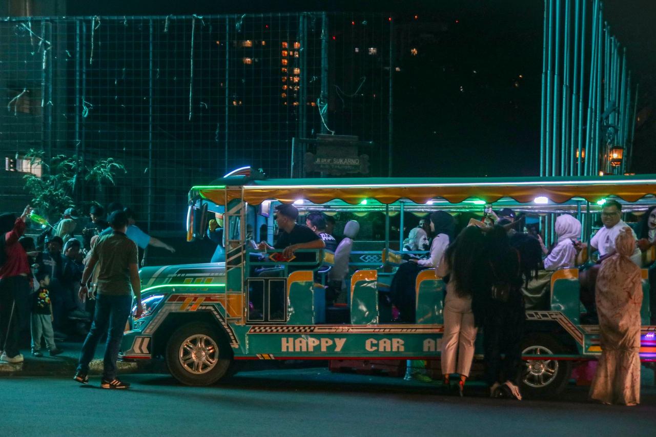 A vibrant night scene with a colorful tour bus and passengers in an urban environment.