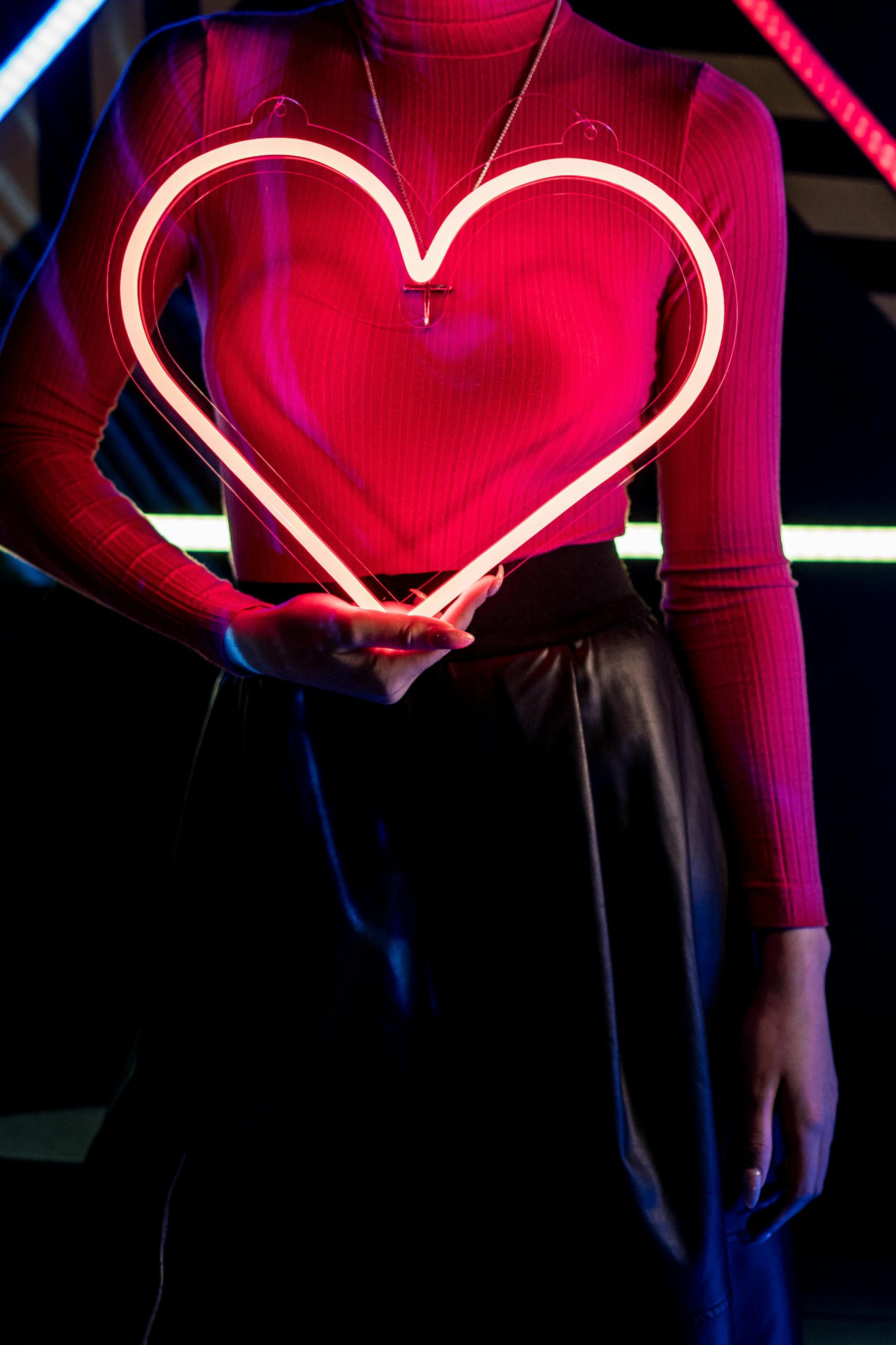 A woman holds a neon heart under vibrant cyberpunk lighting, creating a modern and artistic look.