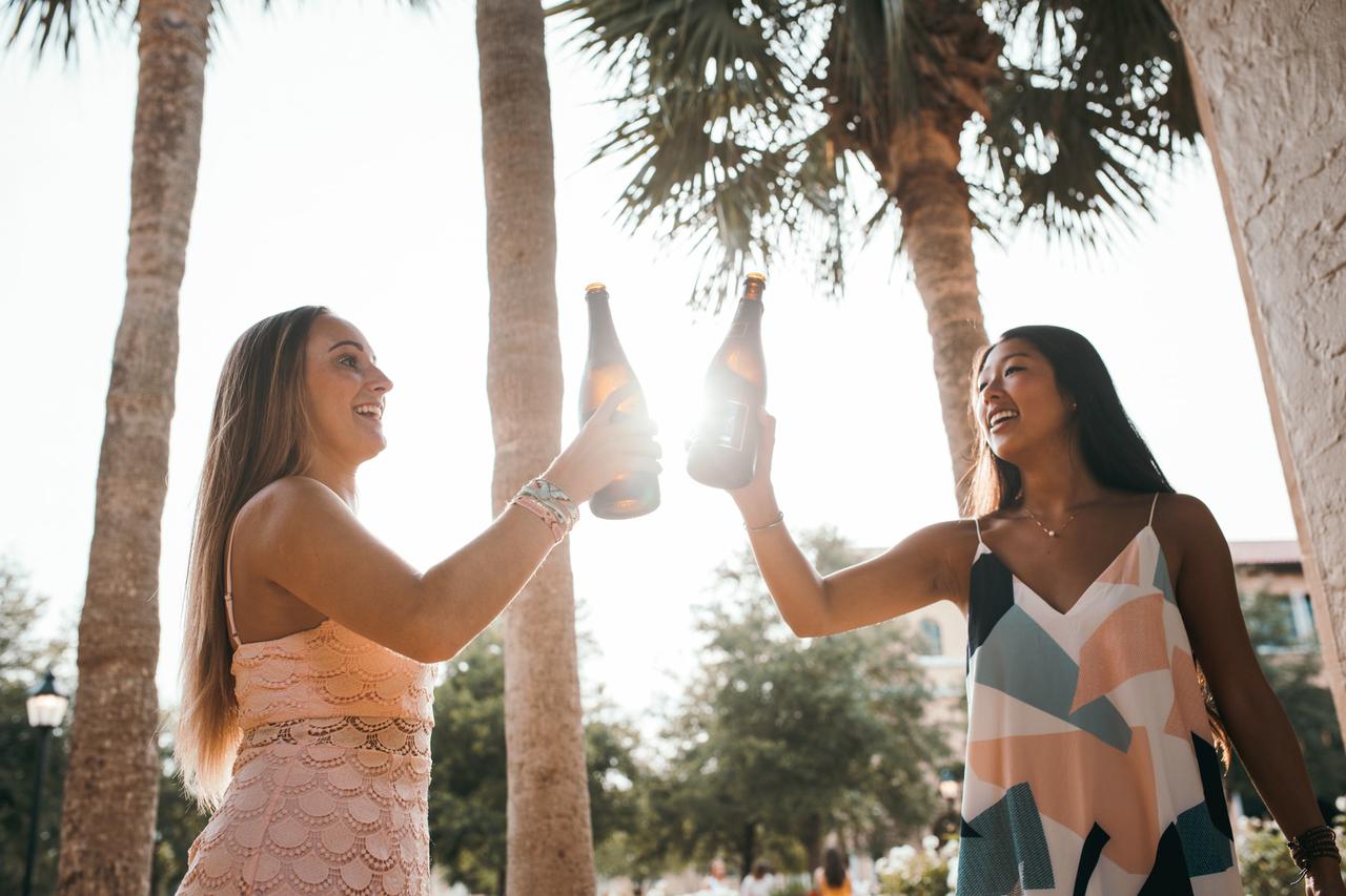 Two girls with beers cheersing to good times. Celebrate Labor Day the right way and rent a party bus.