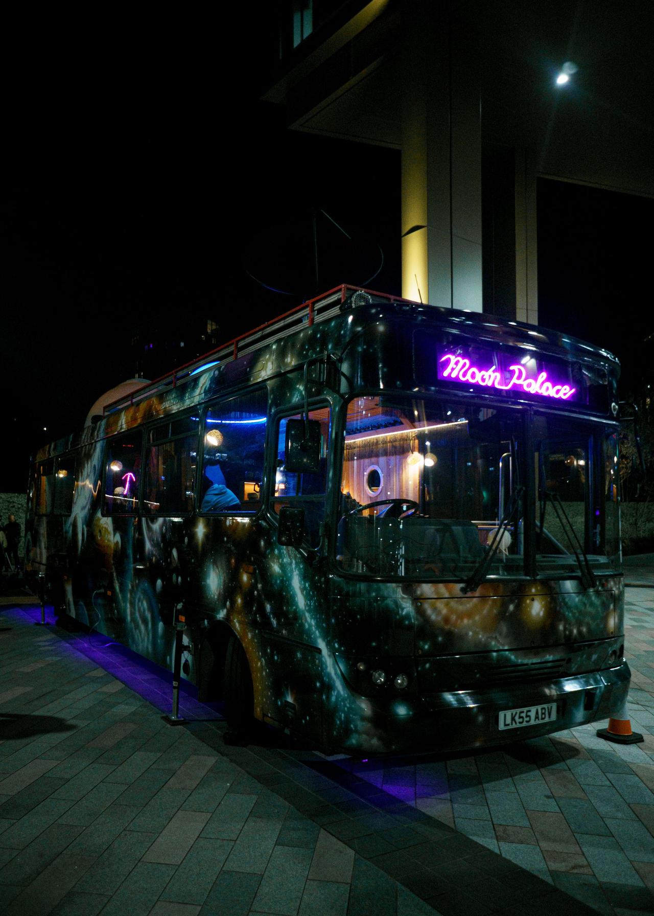 Decorative bus named 'Moon Palace' lit up at night in Leeds city center.