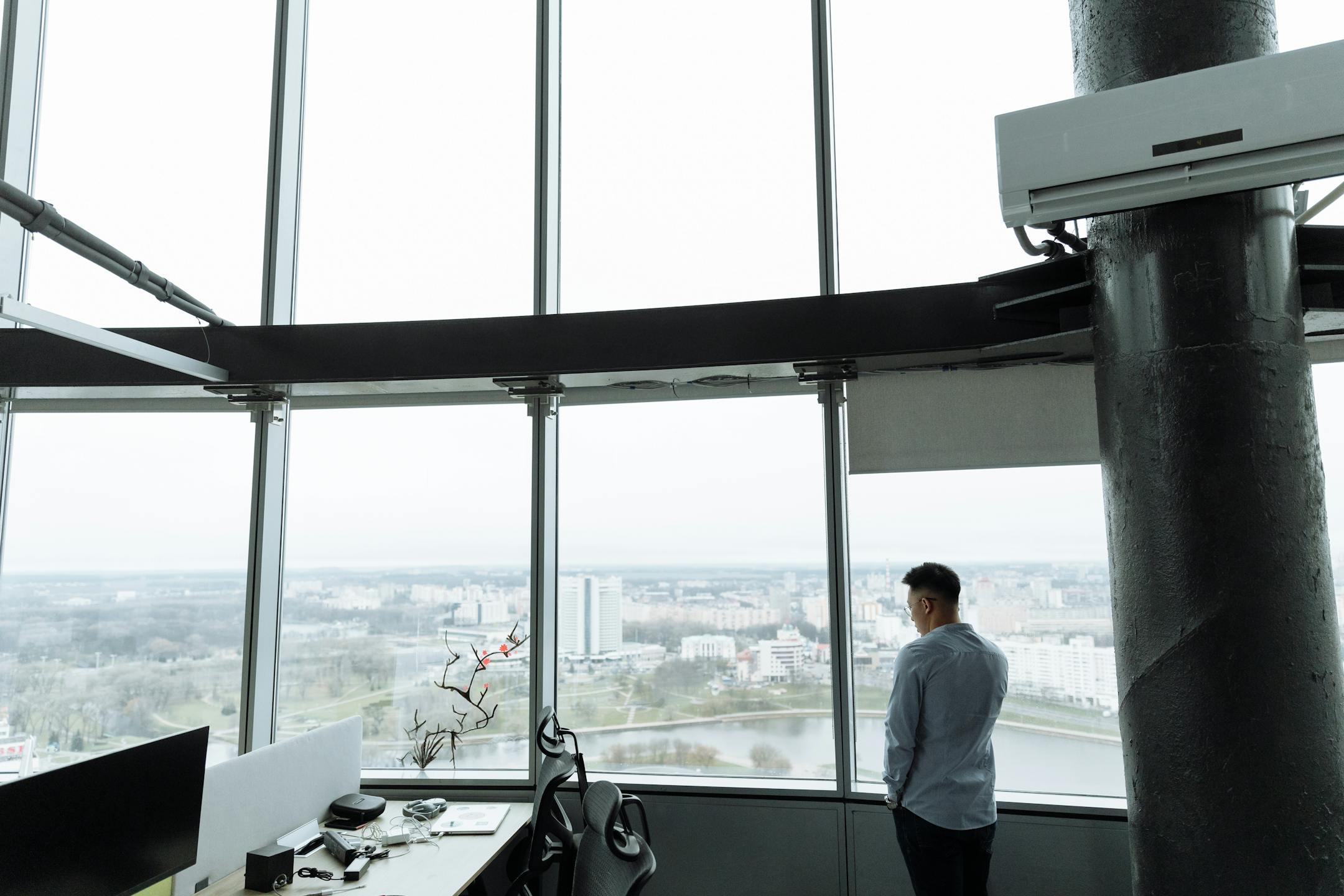 Businessman stands in a high-rise office with a panoramic city view, embodying modern corporate environment.