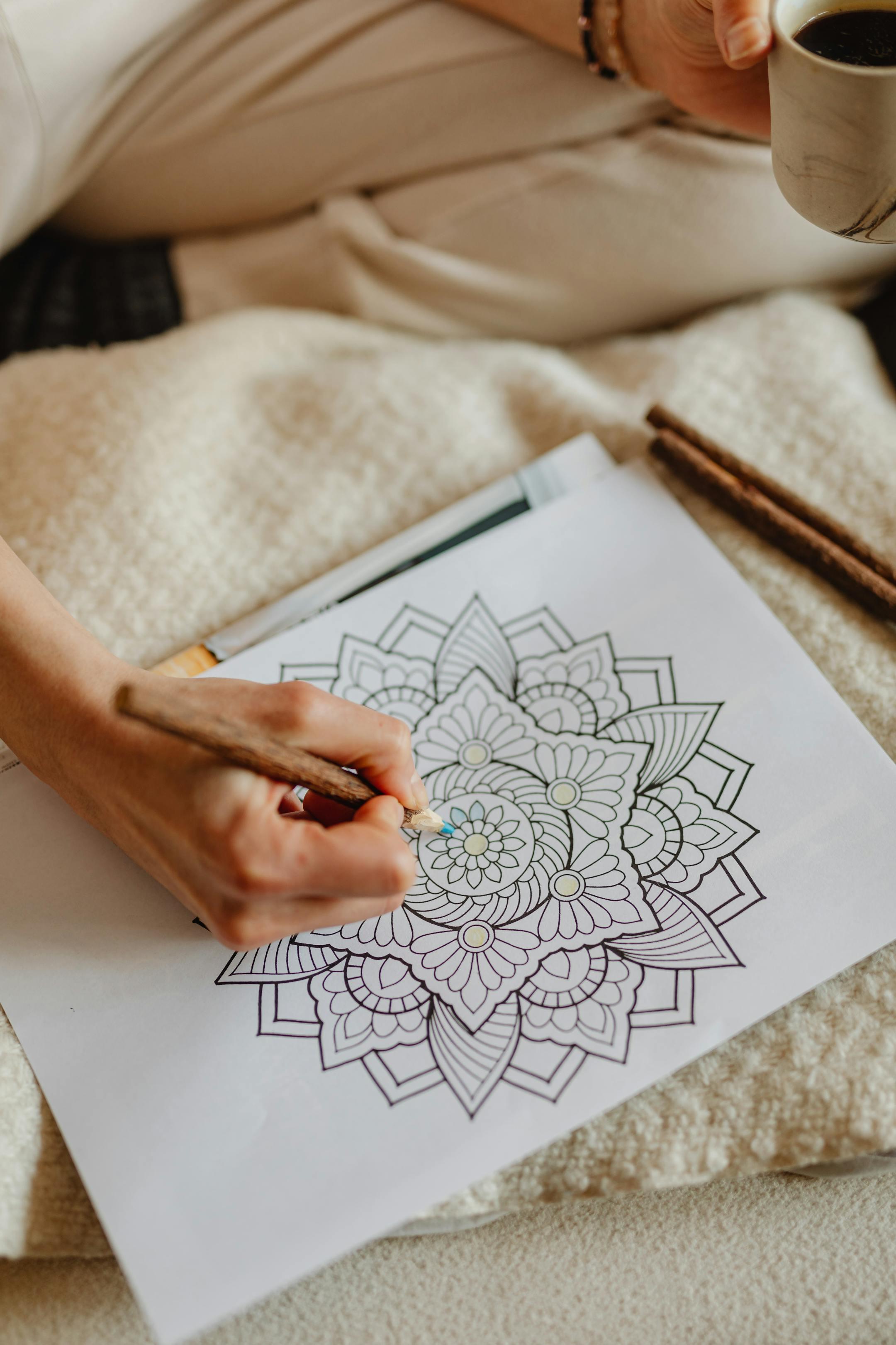 Person coloring intricate mandala design, focused relaxation with coffee mug.
