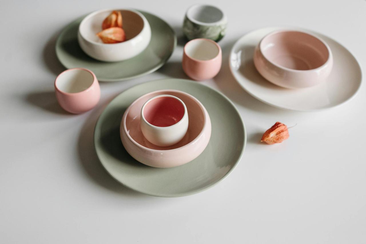 Top view of arranged ceramic plates and cups in pastel colors on a white surface.