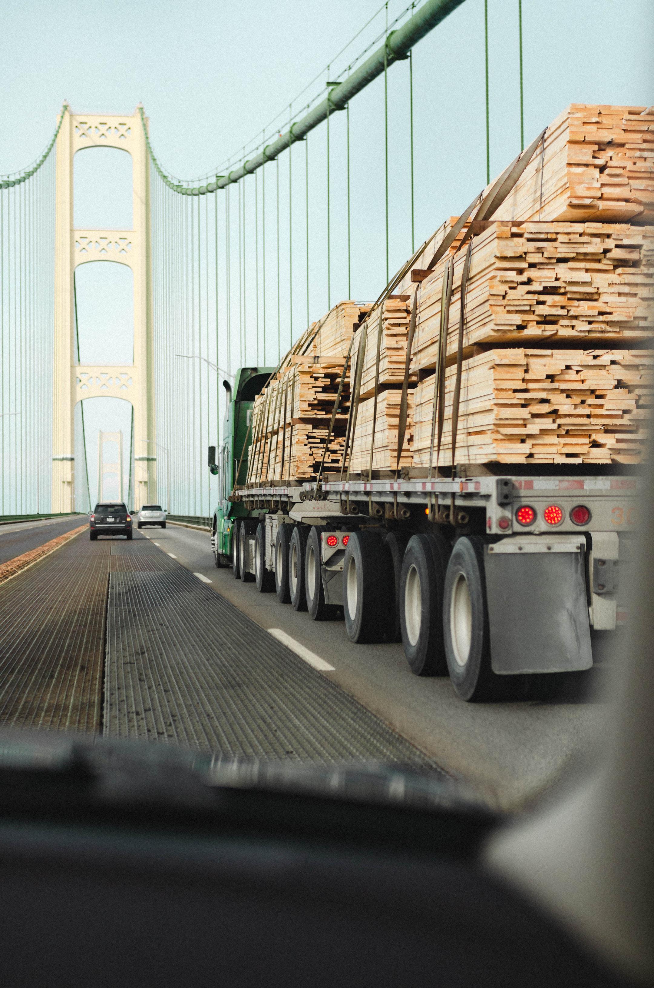 A flat-bed truck transporting wood pallets over a bridge.