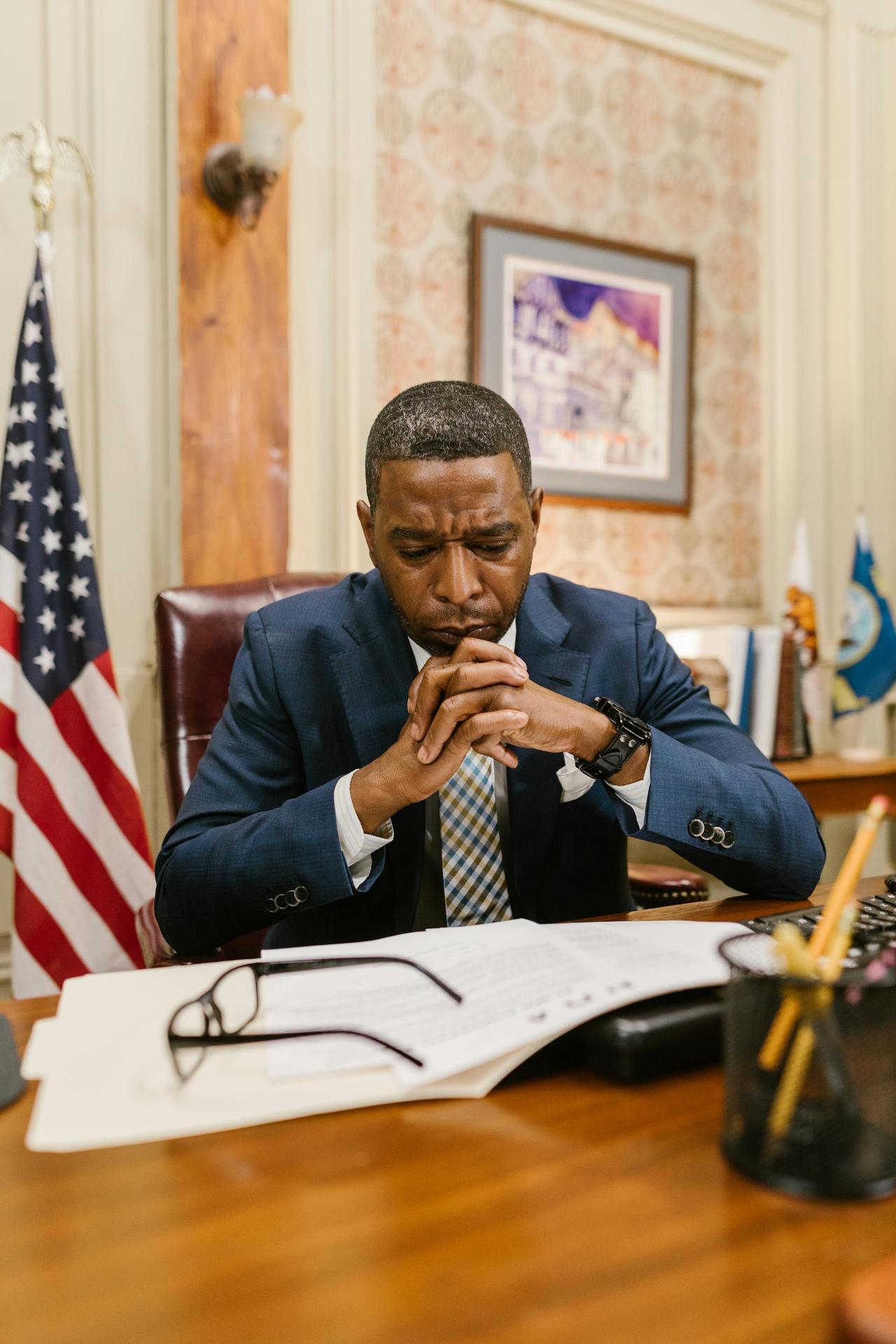 Lawyer in deep thought at office desk with documents and flag.