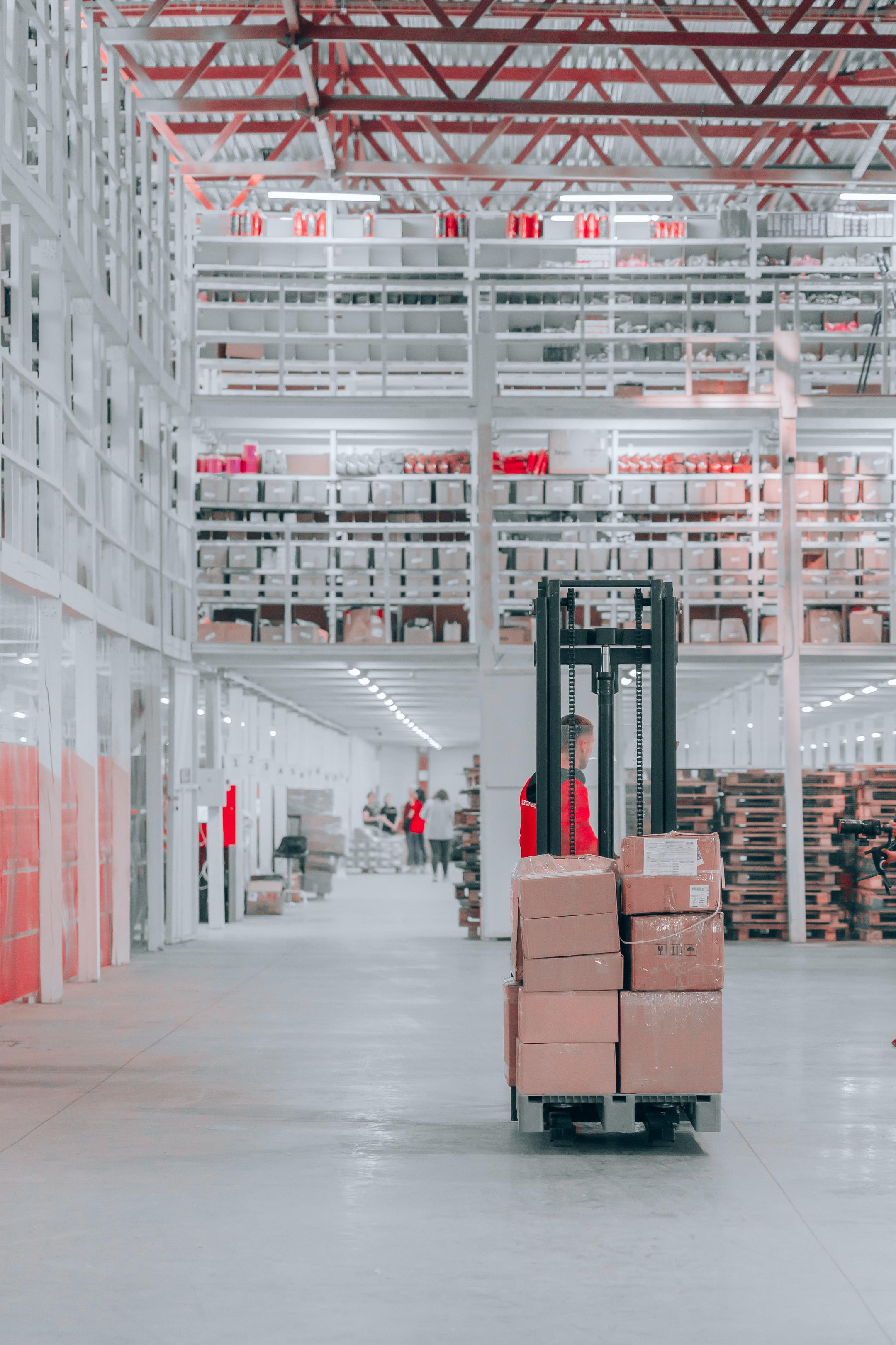 A person operating a standing forklift in a warehouse.