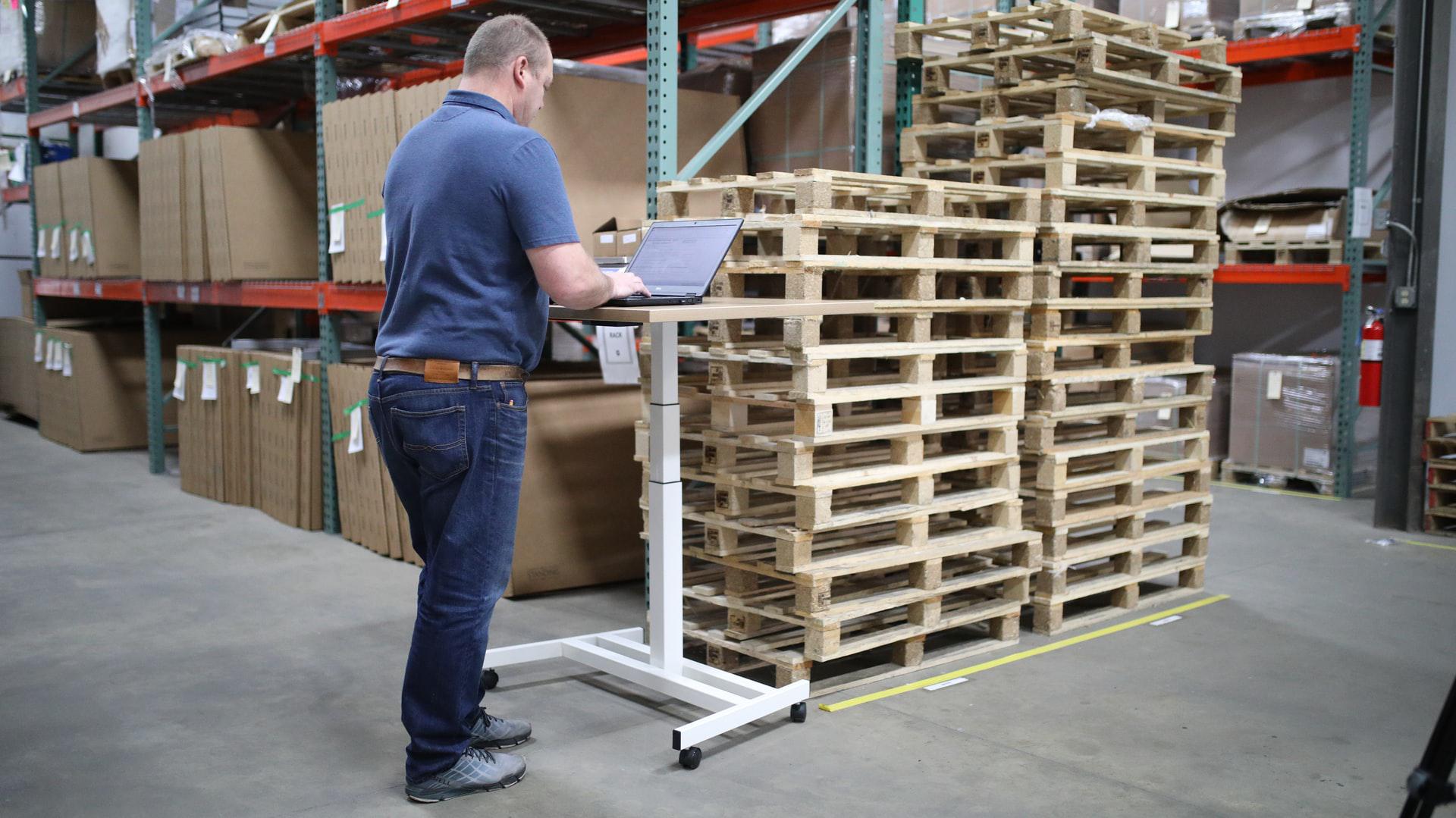 Man with laptop on stading desk in a warehouse