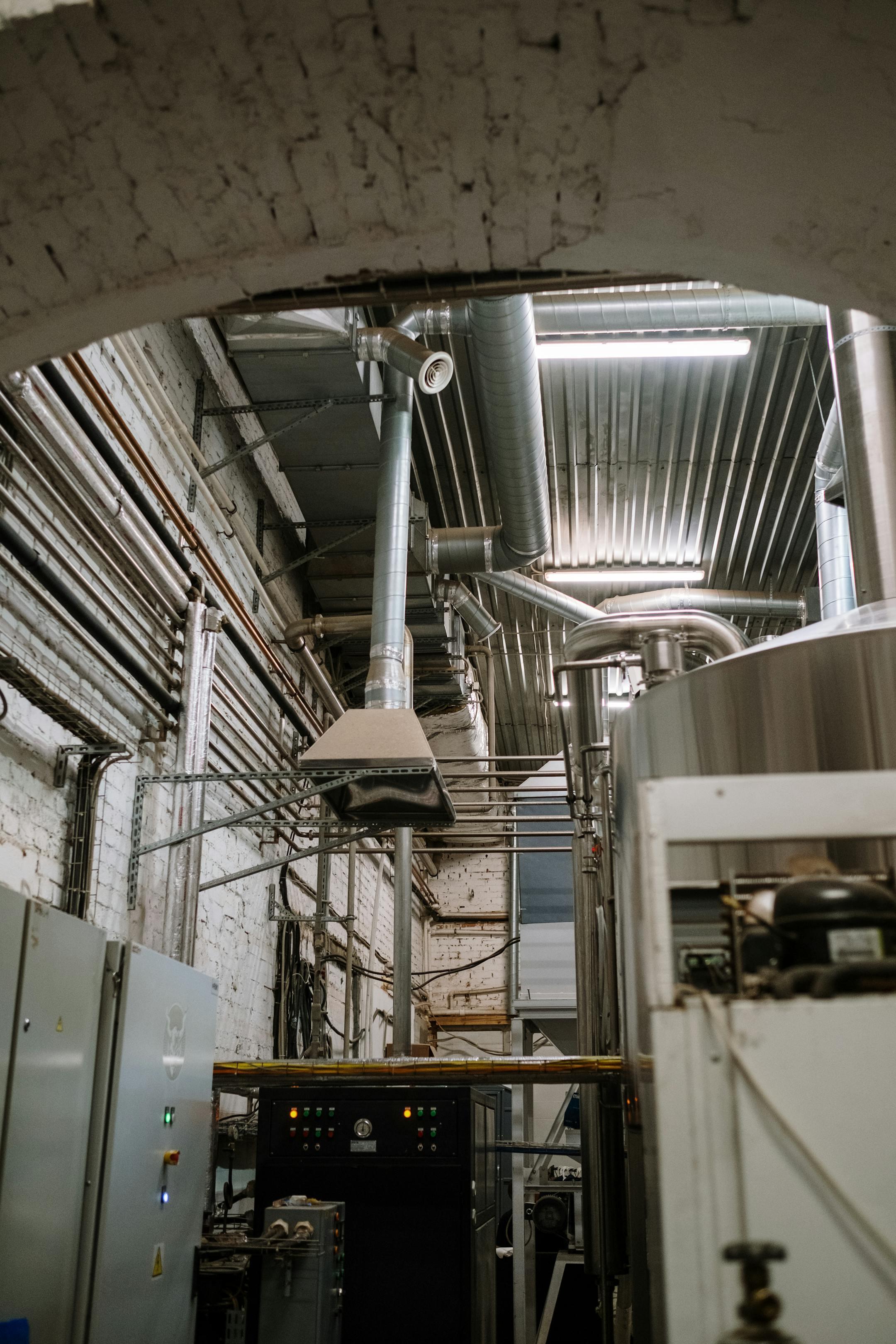 Stainless steel equipment inside a modern industrial brewery with intricate piping and machinery.