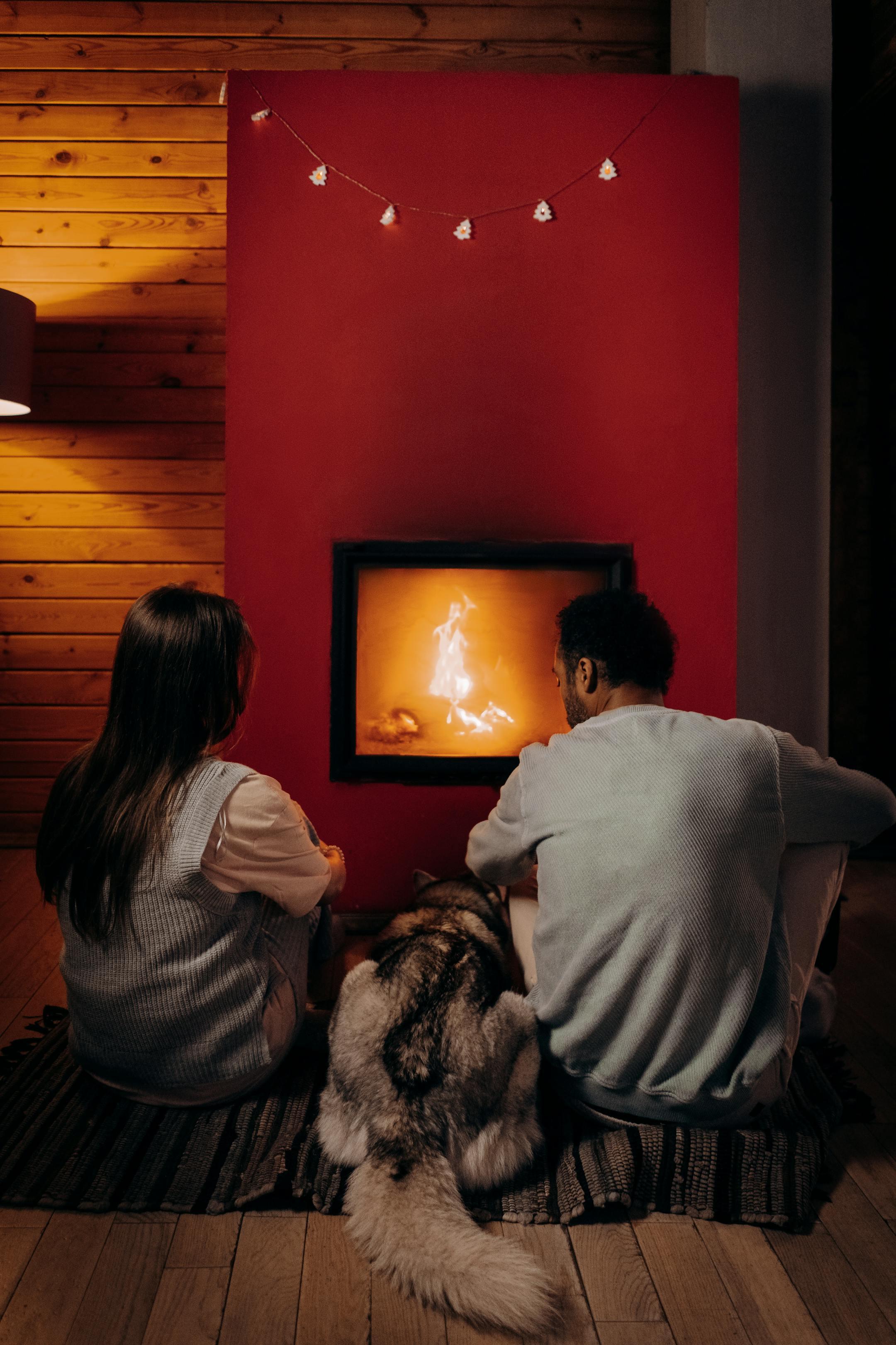 A couple and their dog enjoying a warm evening by the fireplace indoors.