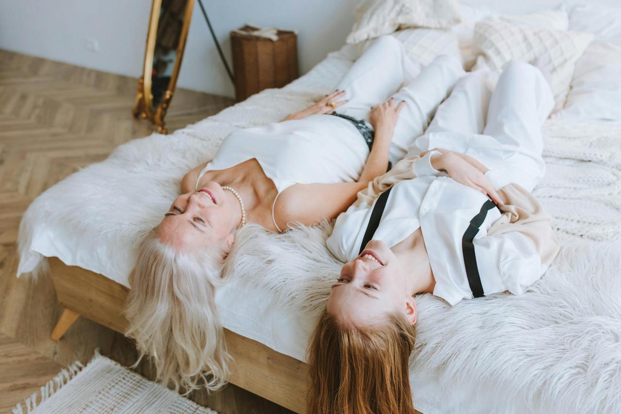 A joyful grandmother and granddaughter relaxing on a cozy bed, enjoying togetherness and good vibes indoors.