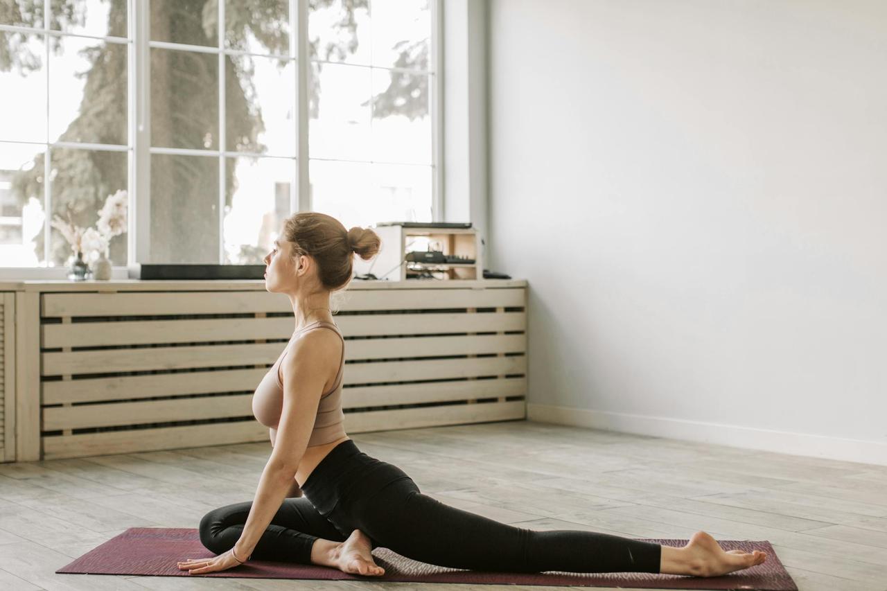 Woman practicing yoga in a sunlit room, embodying flexibility and wellness.