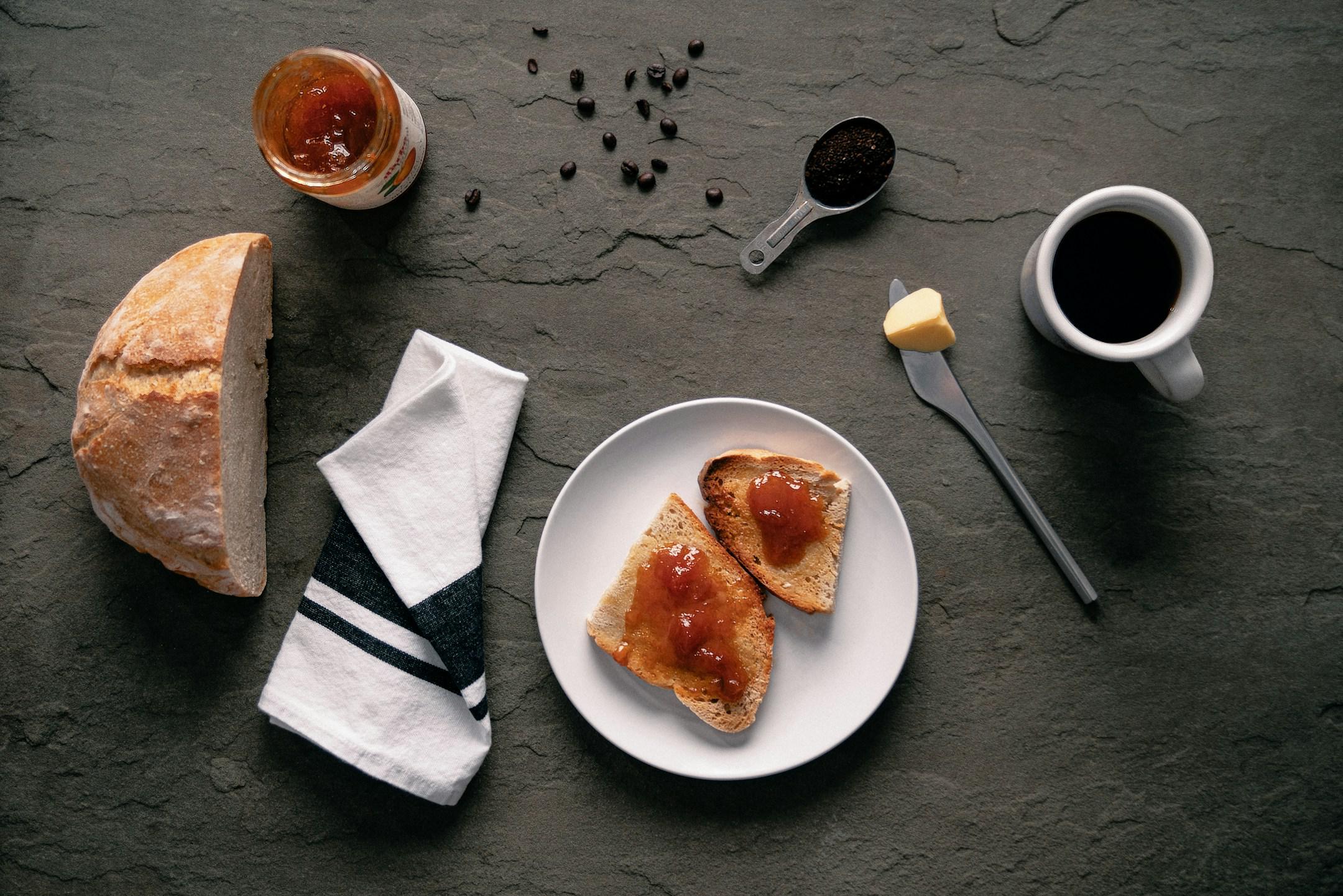 simple breakfast spread with loaf of bread, toast, jam, coffee, and coffee beans artfully arranged.