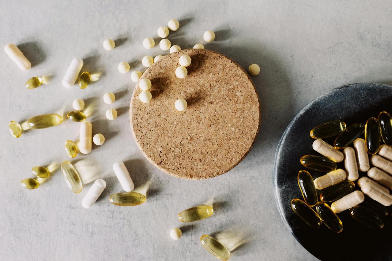 A variety of capsules and tablets scattered on a cork and plate, representing healthcare and wellness.