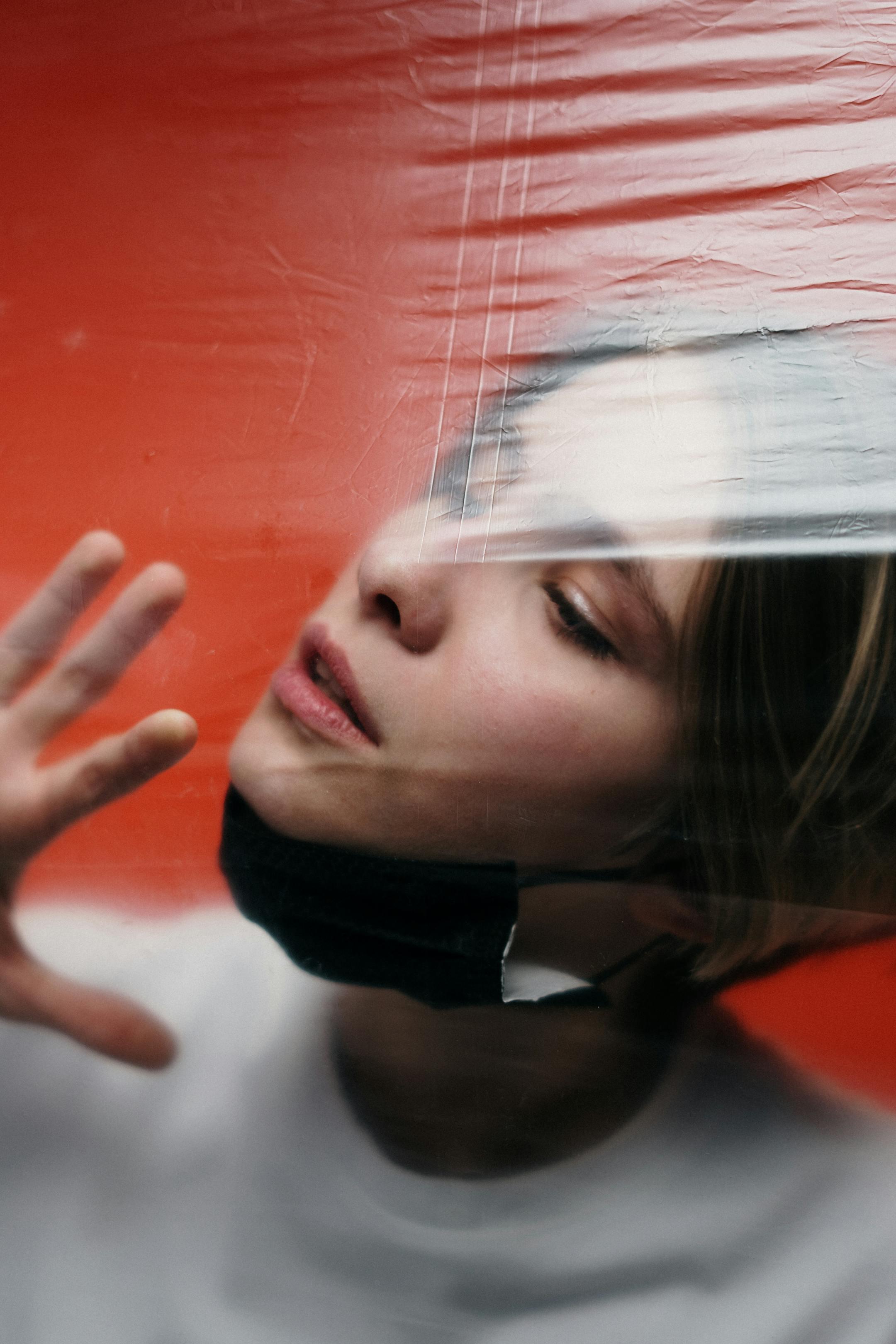 Portrait of a woman wearing a face mask, touching plastic, symbolizing isolation.