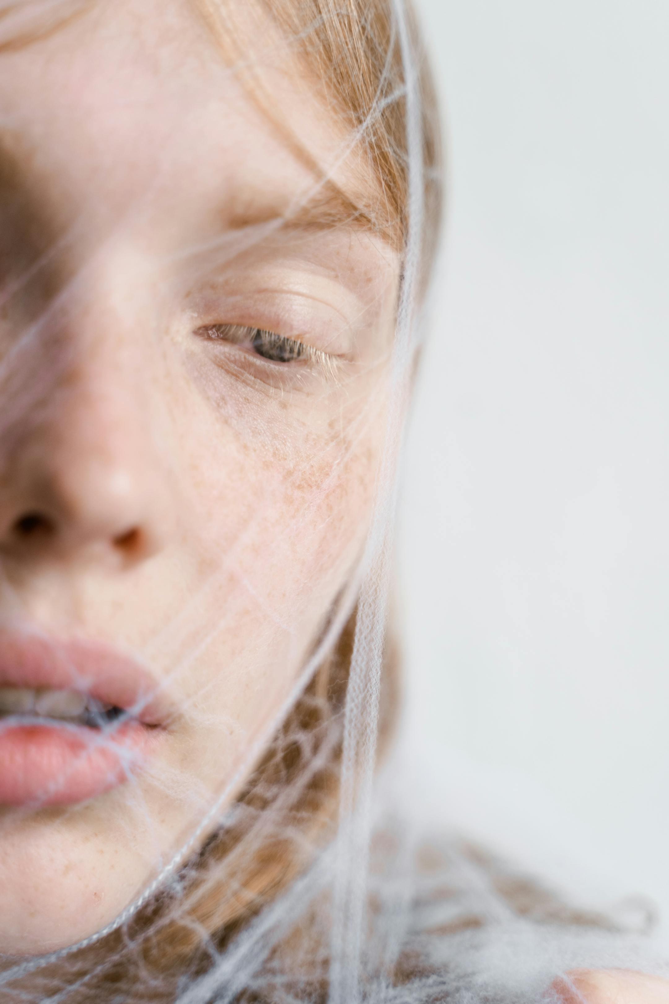 A delicate and ethereal close-up portrait of a woman enveloped in a spider web-like texture.
