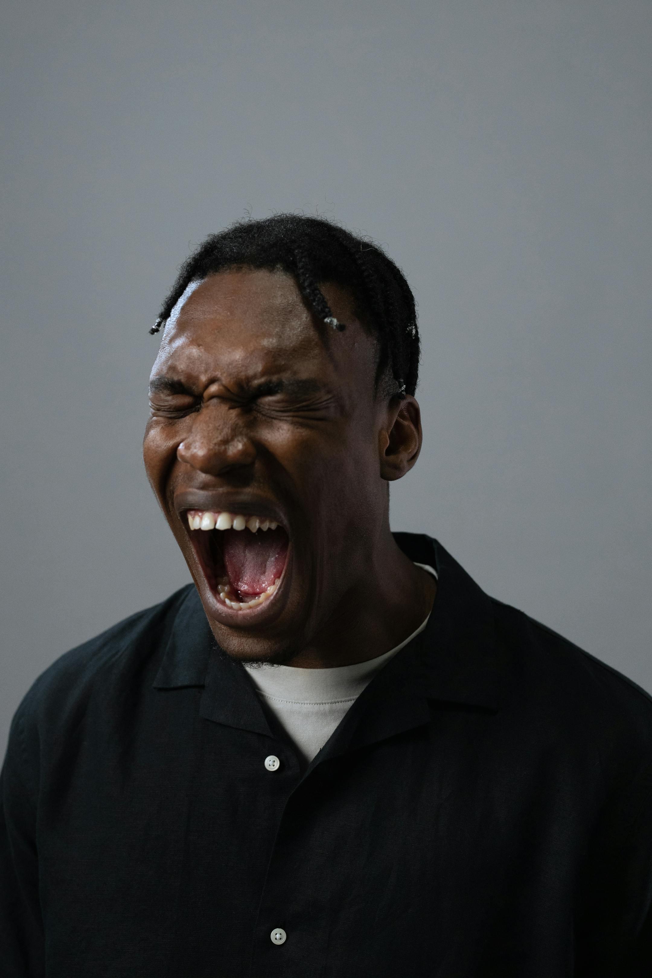 Powerful portrait of a man with braided hair expressing intense emotion against a gray backdrop.