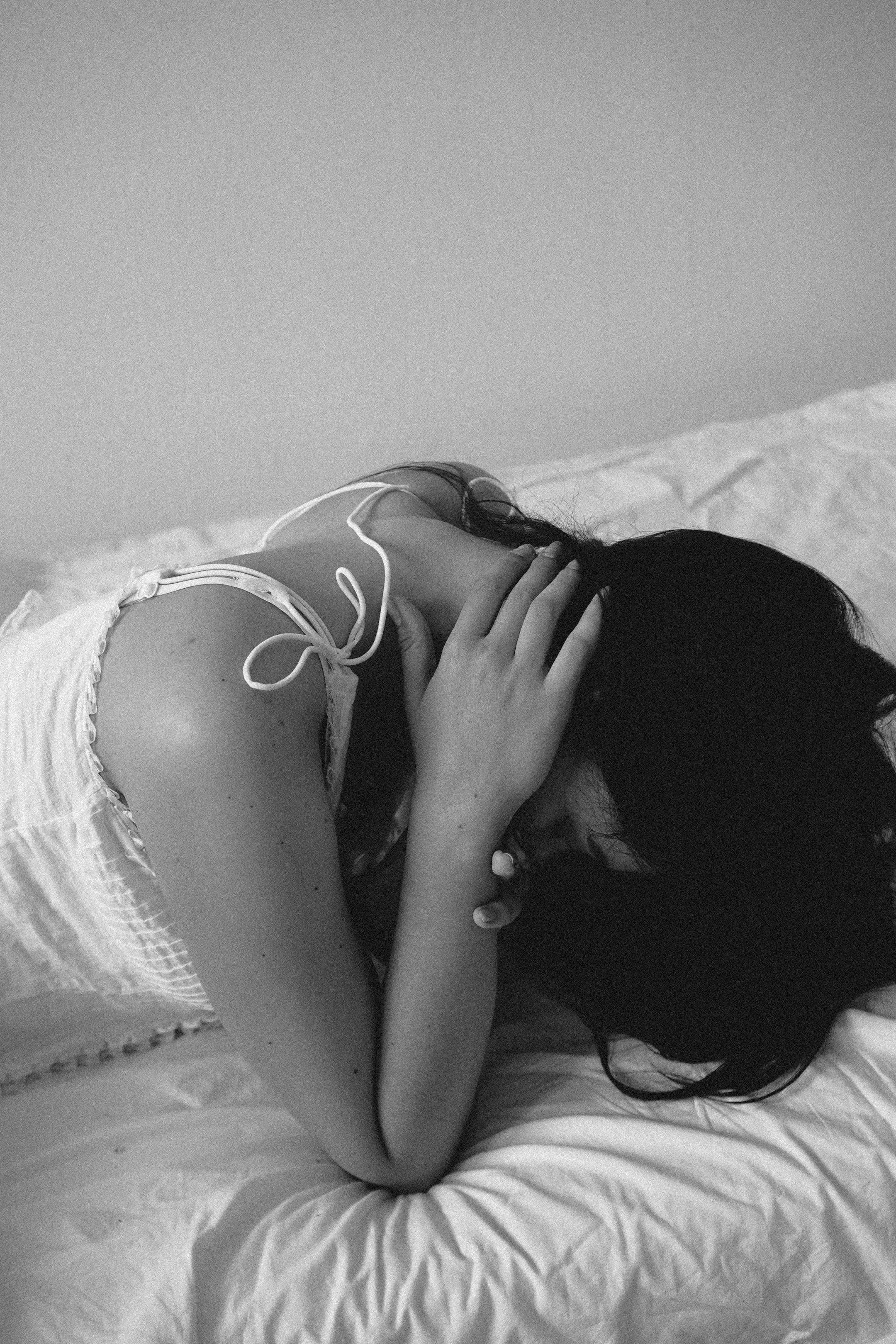 Black and white portrait of a woman in distress, lying on a bed.