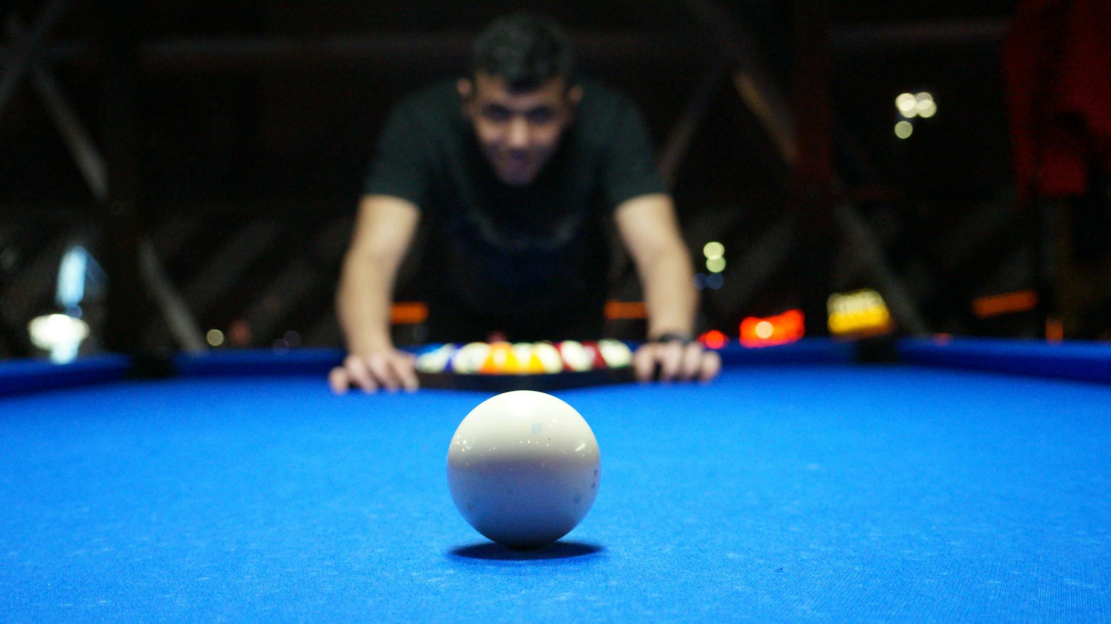 A focused shot of a cue ball on a pool table with a player prepared for a break shot.