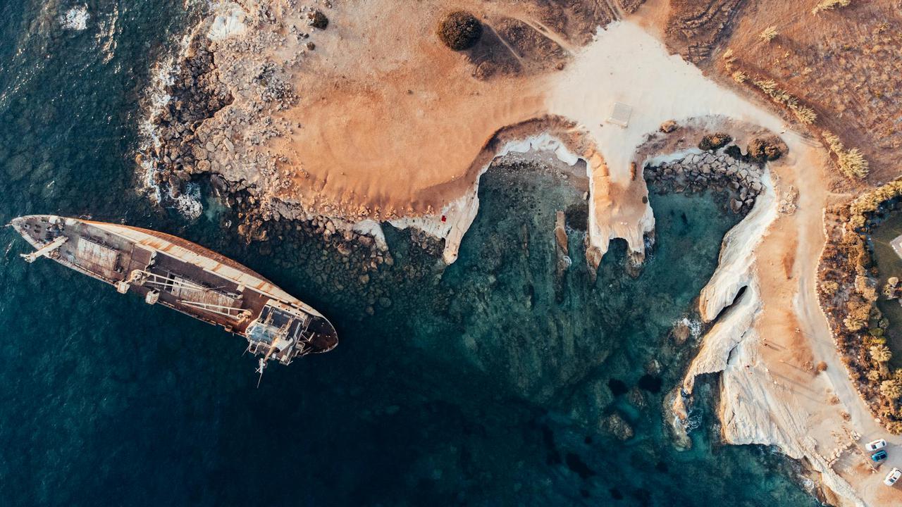 Dramatic aerial shot of a shipwreck on Cyprus's rocky shoreline at daytime, showcasing natural beauty.