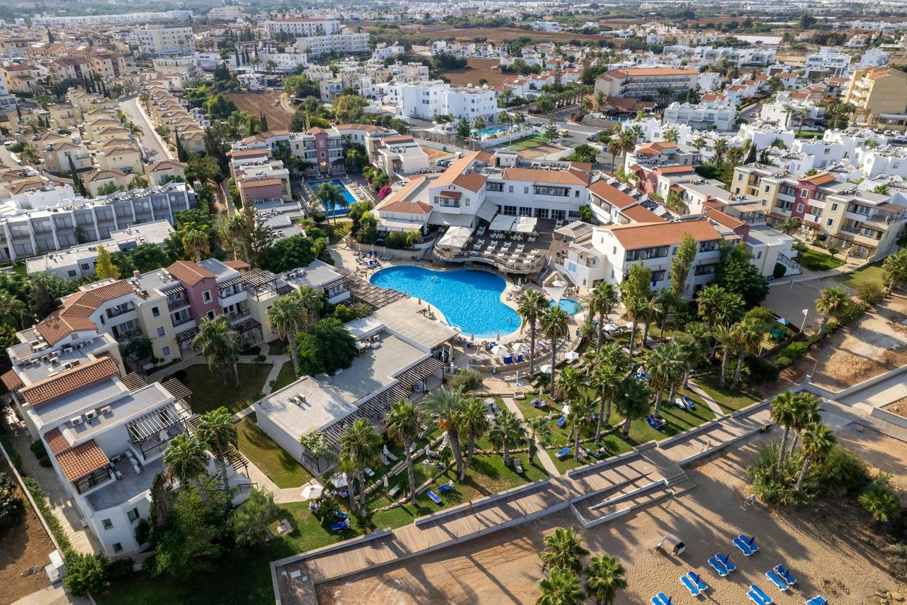 Aerial shot of a scenic resort with swimming pool in Protaras, Cyprus, featuring palm trees and nearby buildings.