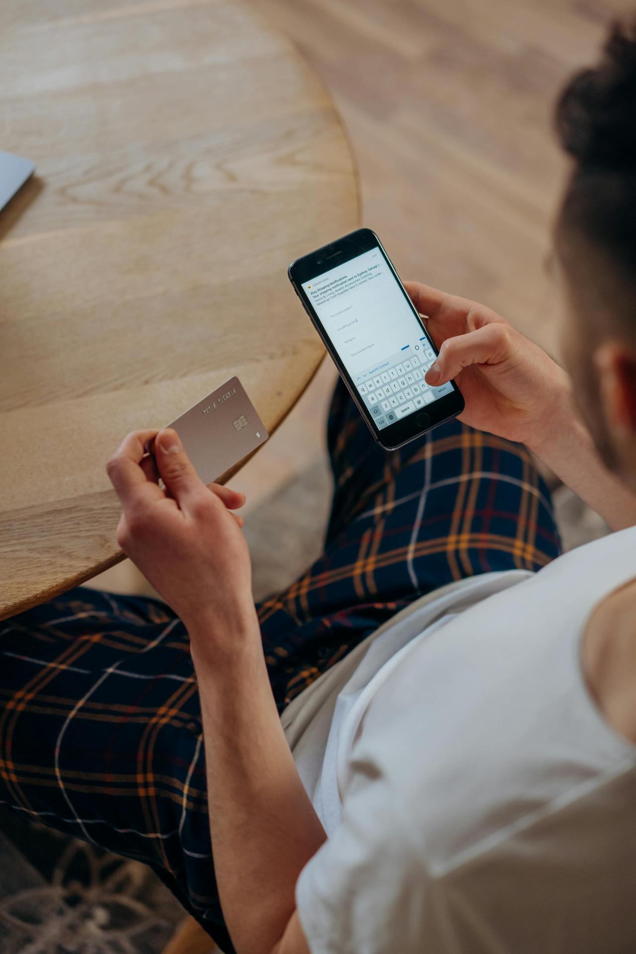 Adult male using a smartphone and credit card for online shopping while sitting indoors. Overhead view.