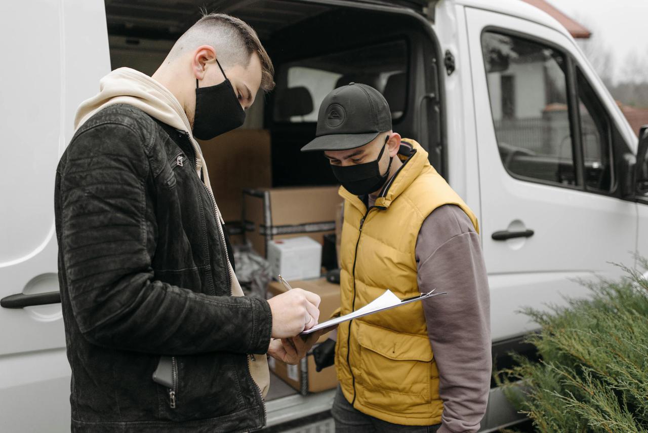 Masked individuals sign paperwork for a courier delivery beside a van. Safe, efficient logistics.