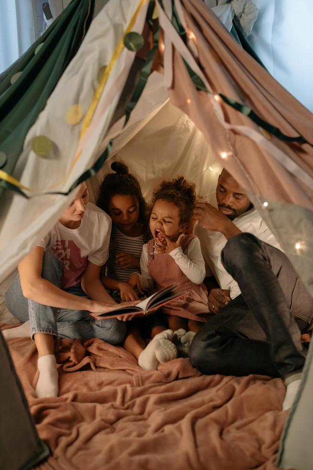 A diverse family reading together inside a cozy, indoor tent, creating a warm and joyful atmosphere.