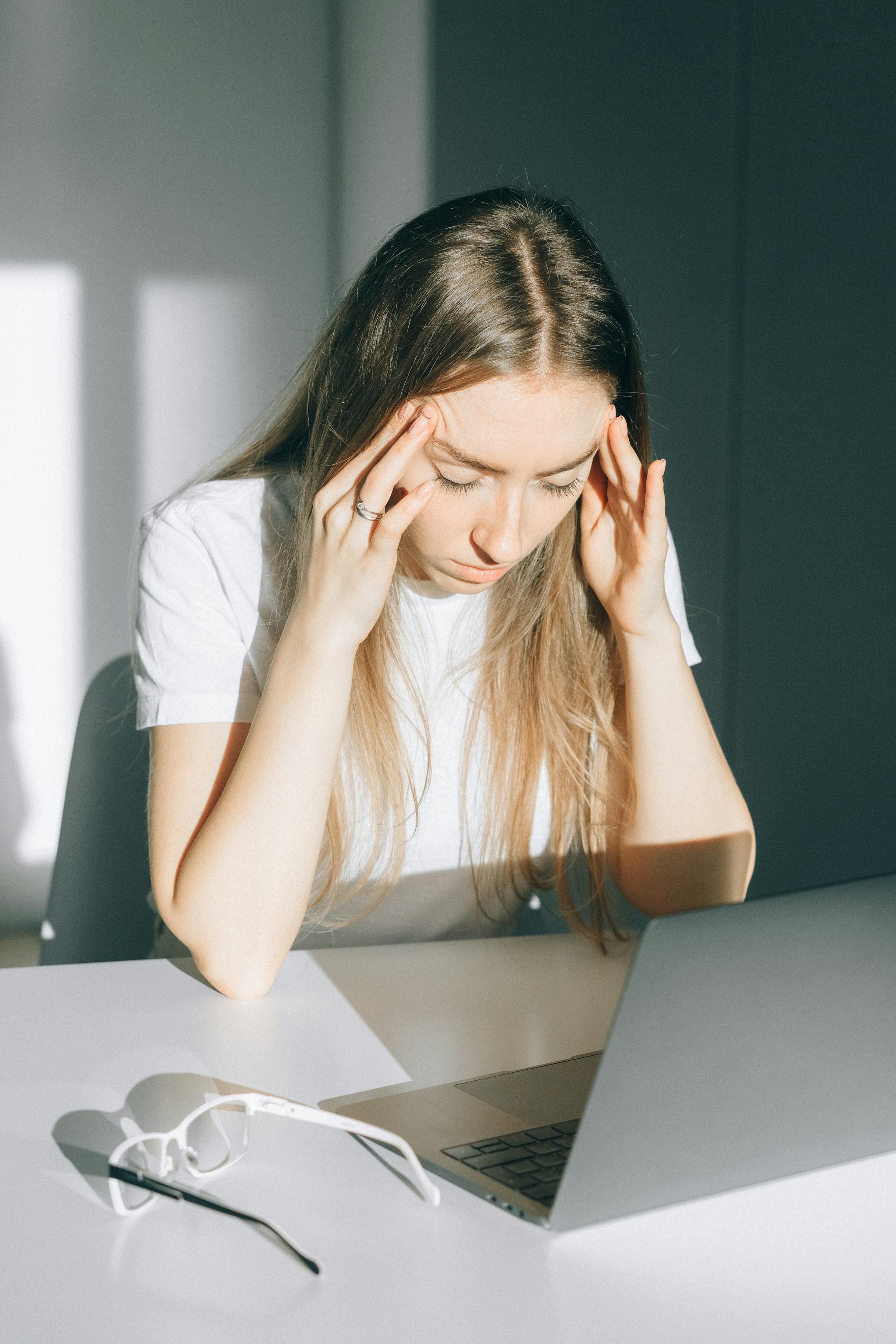 Stressed young woman with a headache working on a laptop indoors.