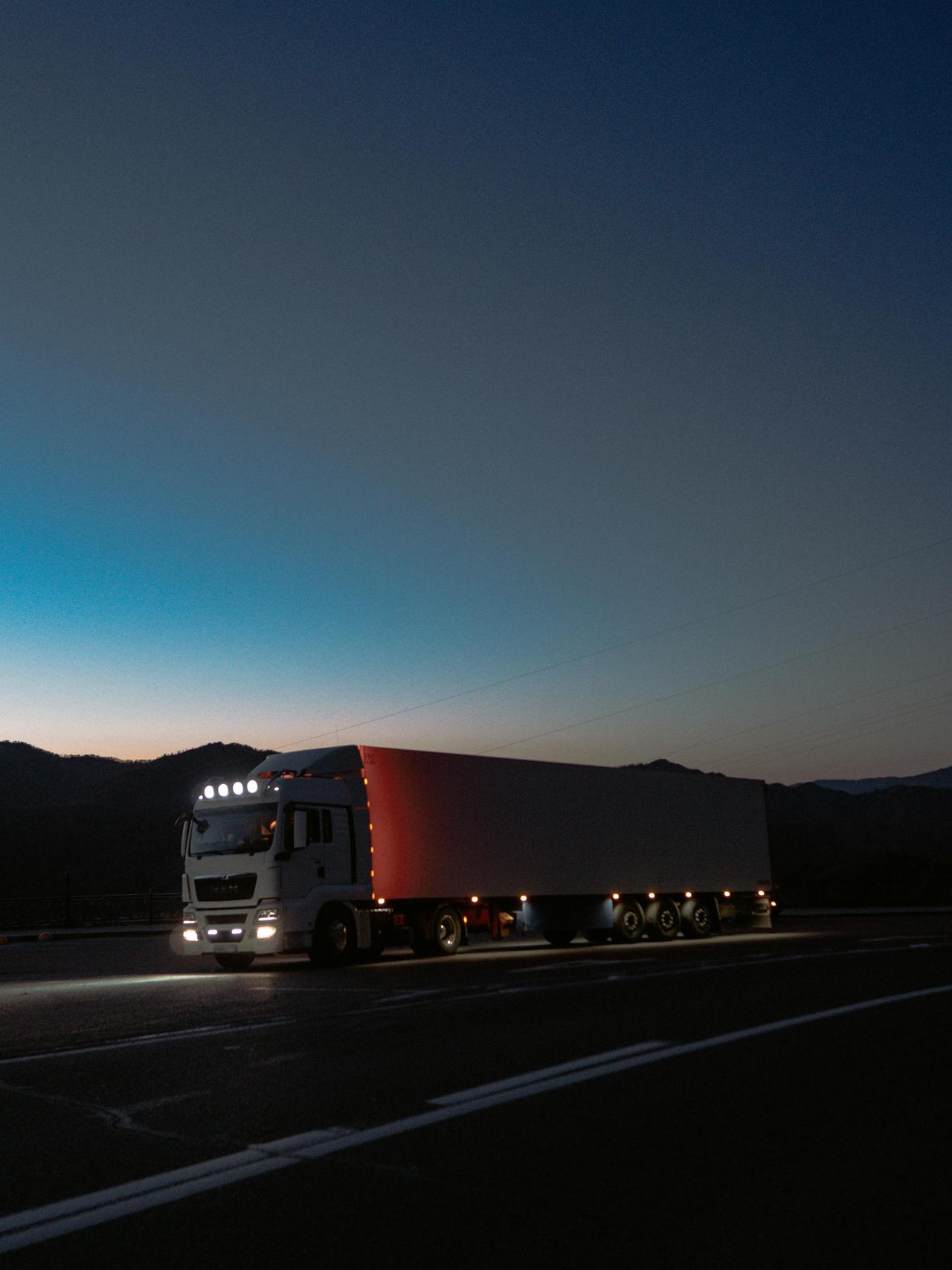 A large truck travels on a highway at dusk surrounded by mountains, showcasing travel and logistics.