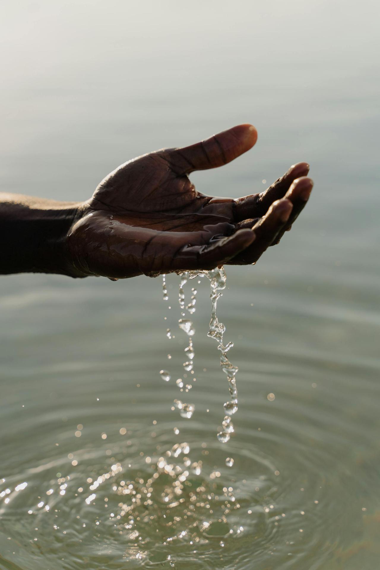 A close-up of a hand with water droplets falling outdoors, reflecting serenity and nature.