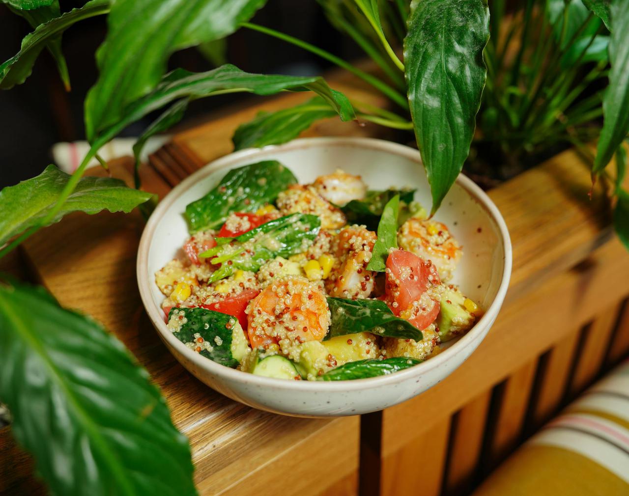 Colorful quinoa salad with fresh veggies in a ceramic bowl surrounded by green leaves.