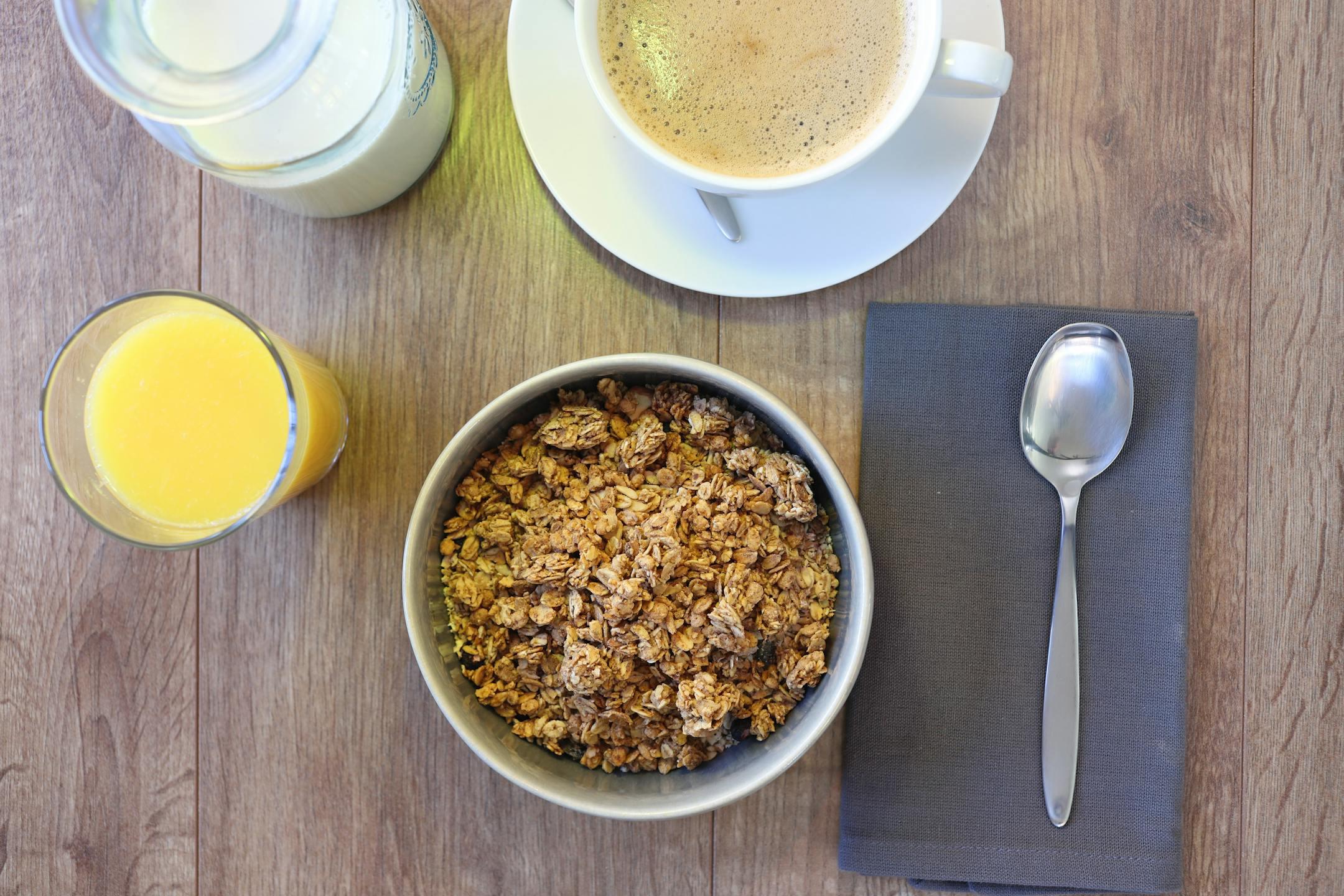 Top view of a breakfast setting with coffee, granola, and juice on a rustic table.